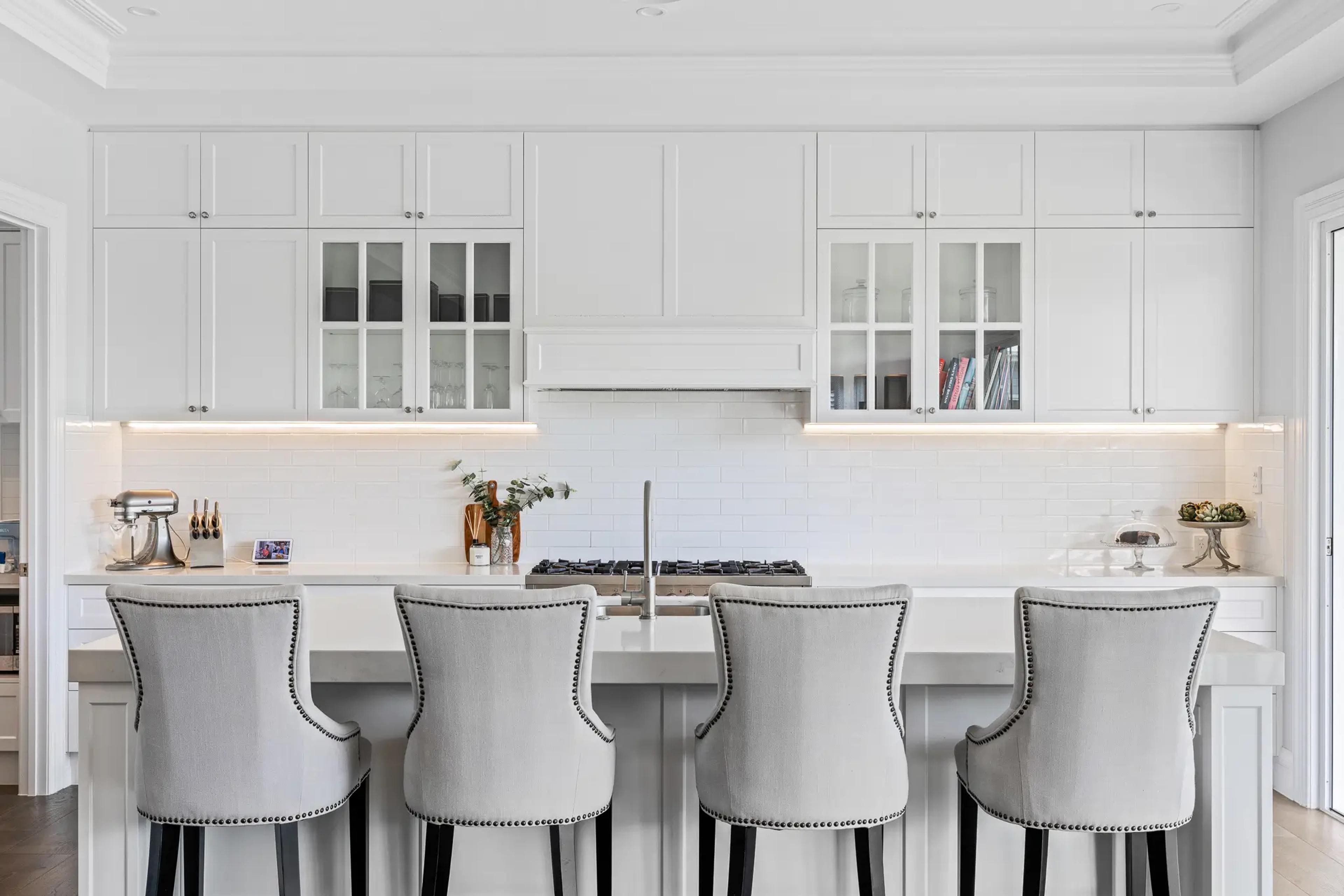 White Hamptons kitchen with island bench and grey upholstered bar stools