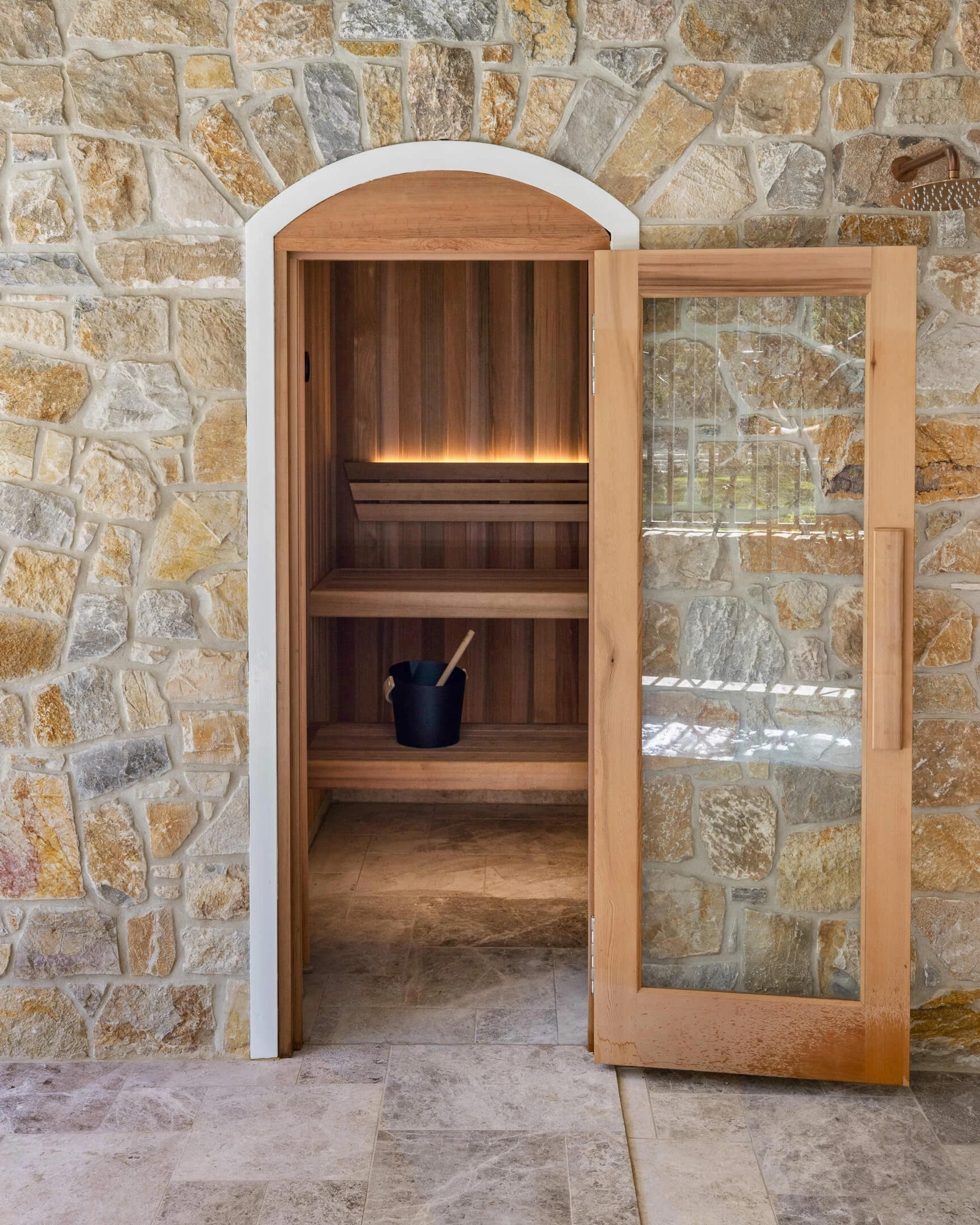 Timber sauna with arched glass door in stone wall