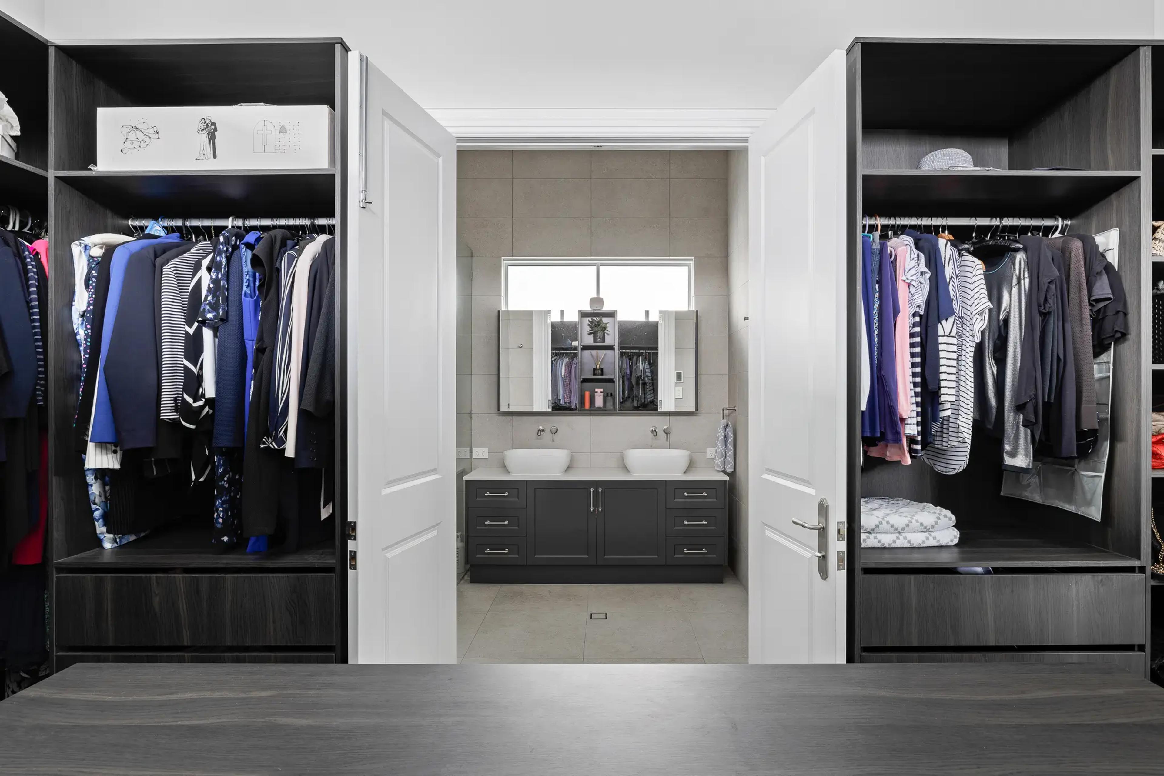 Walk in wardrobe with dark cabinetry leading to twin vanity ensuite