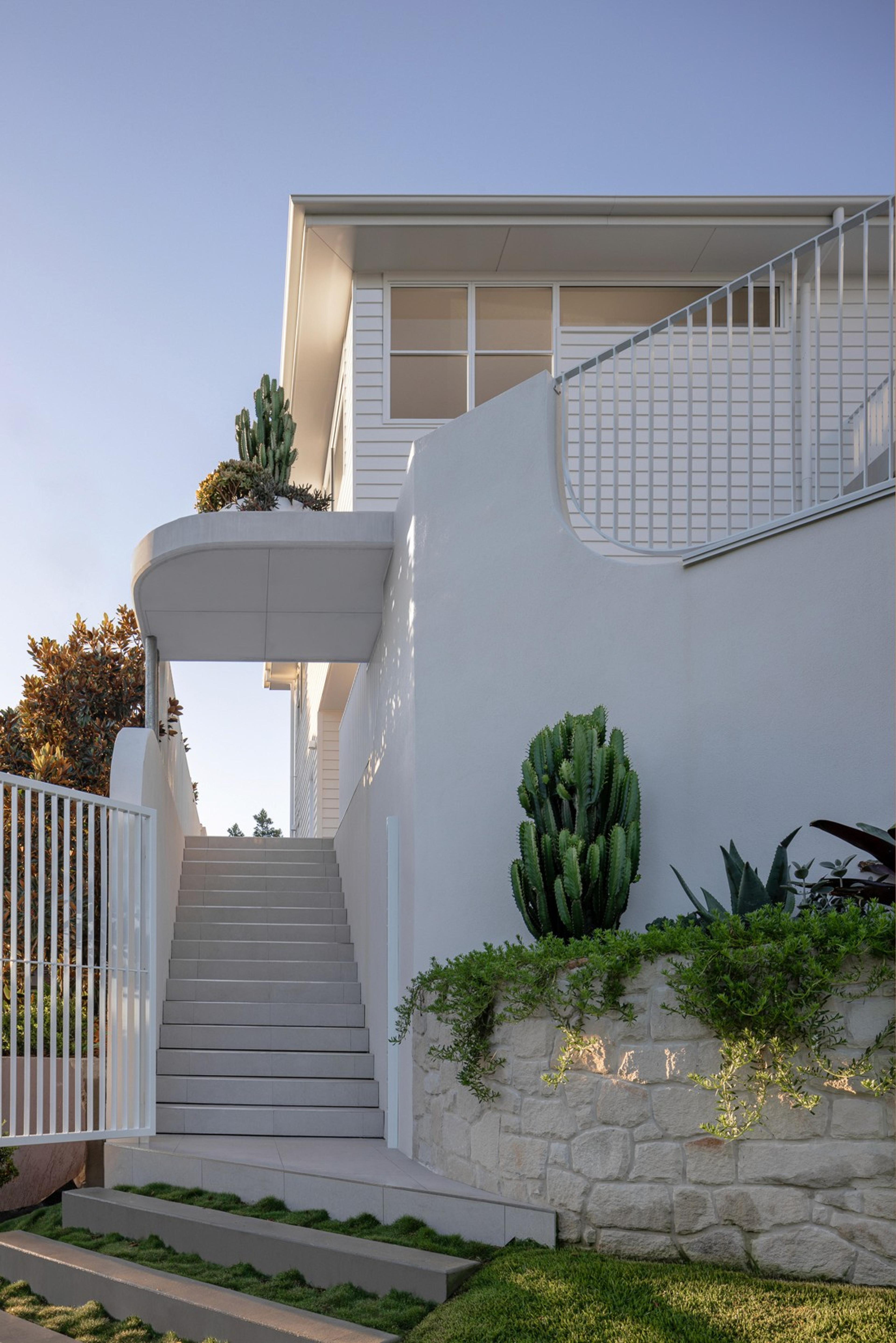 External stairs beside white facade with cacti and stone wall