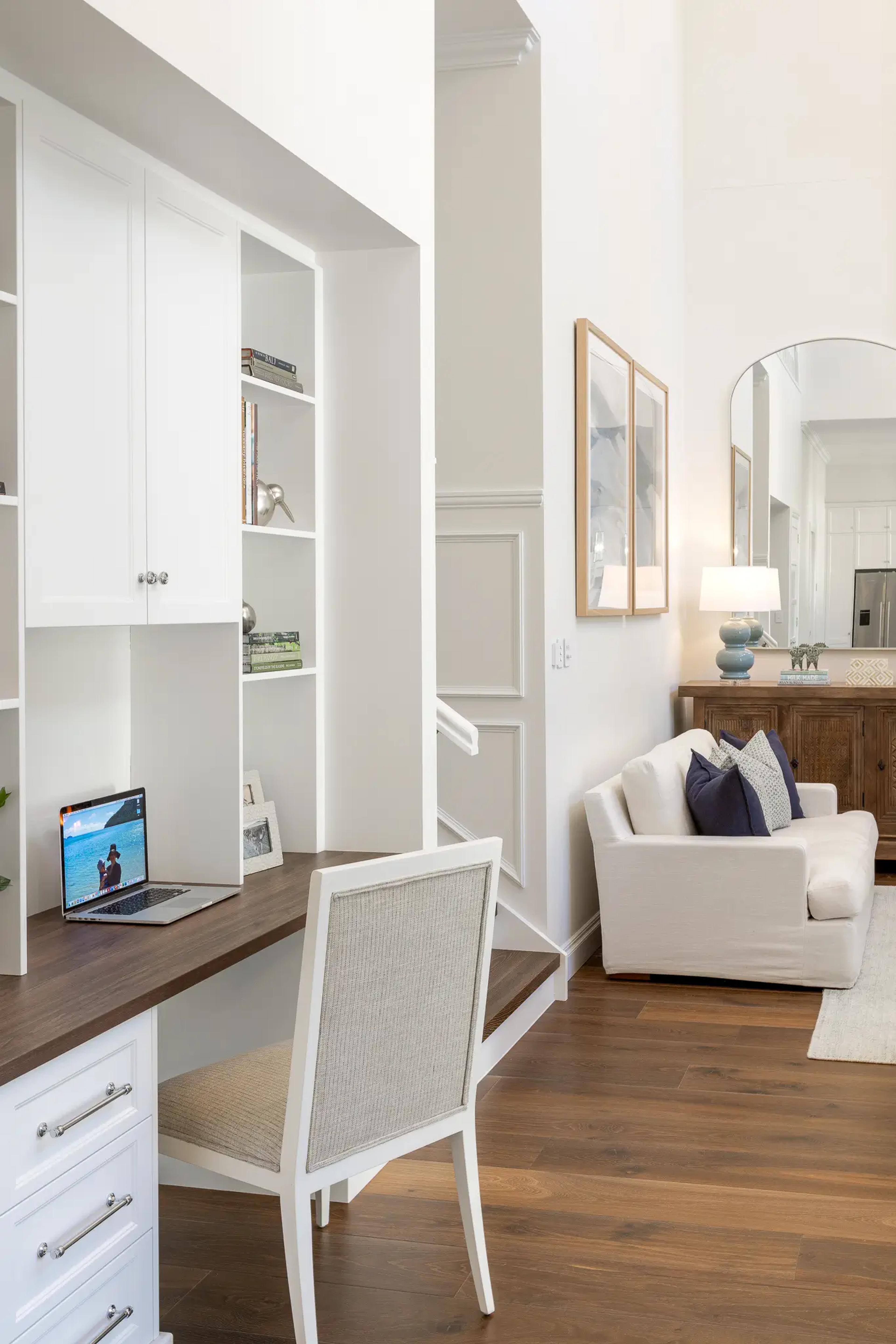 Built in study nook with white cabinetry beside a sitting area and staircase