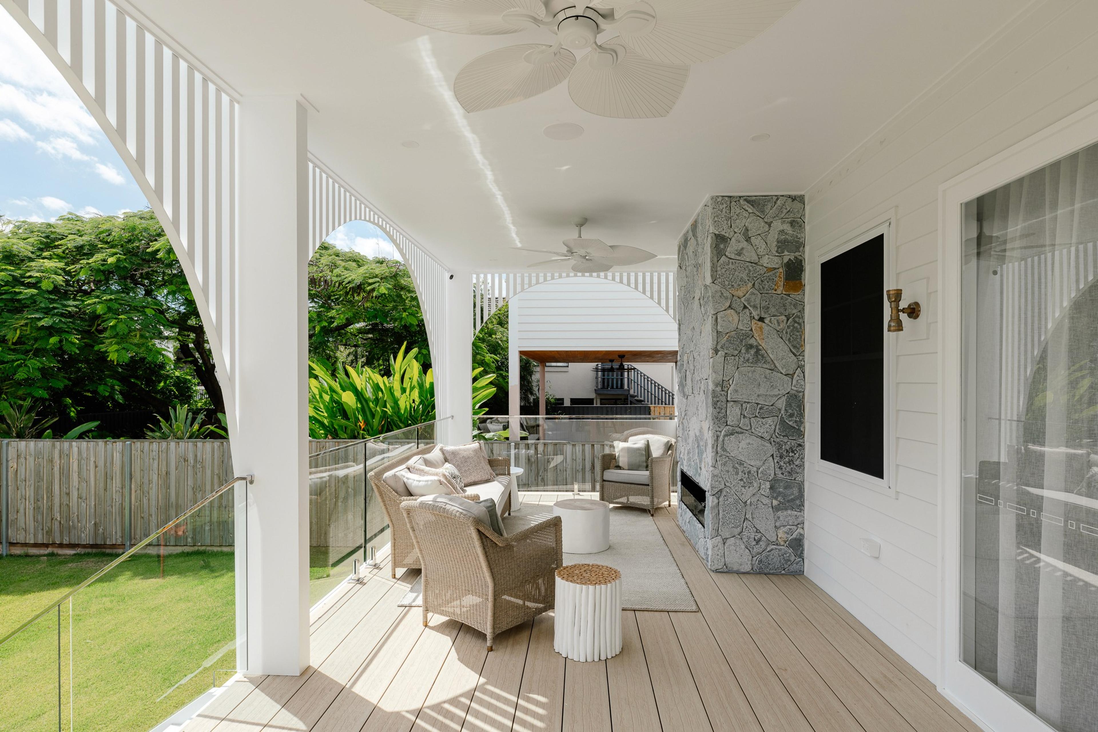 Covered rear verandah with stone fireplace, lounge chairs and garden view