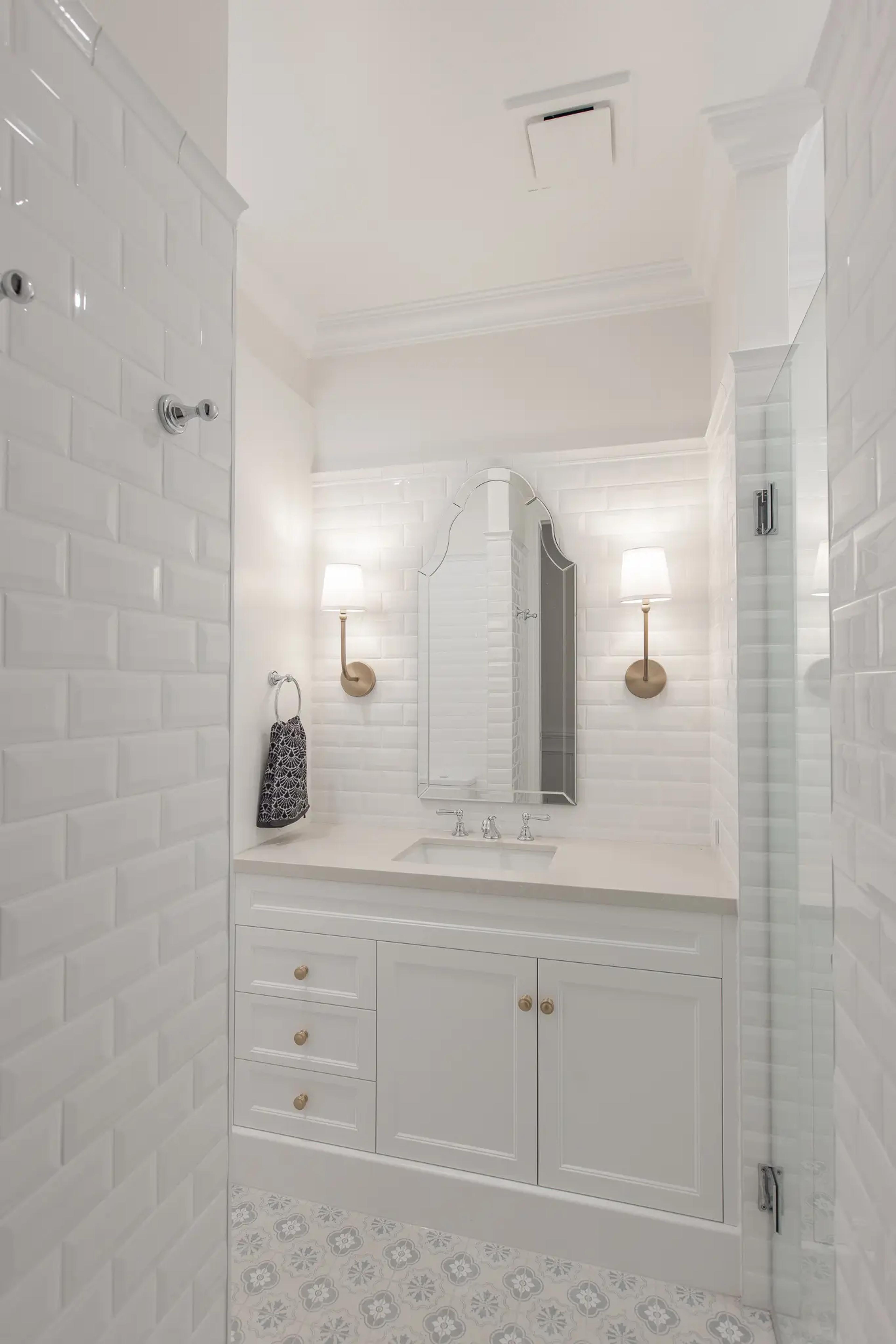 White subway tiled ensuite with vanity, arched mirror and wall sconces