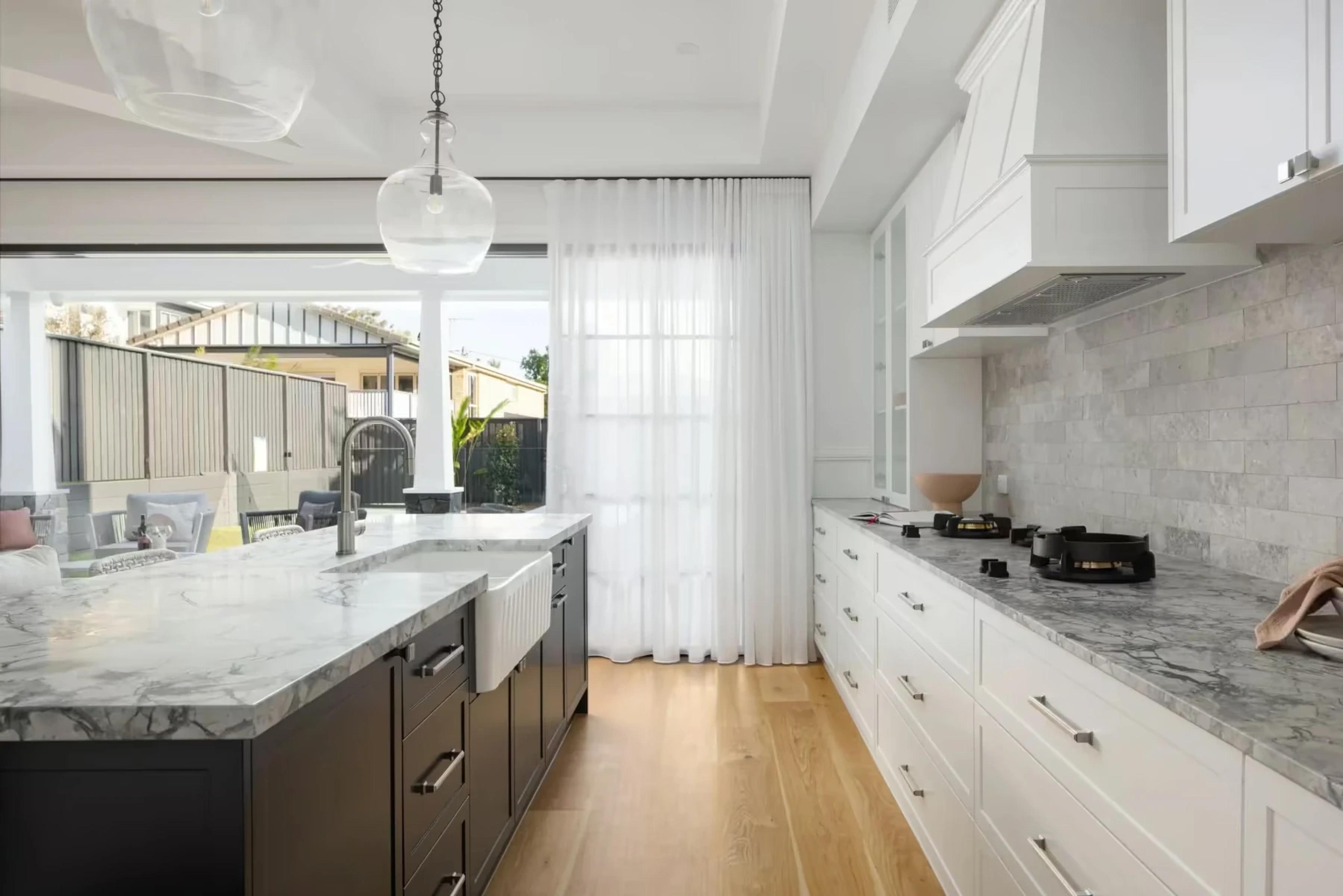 White kitchen with marble island, sheer curtains and timber floors