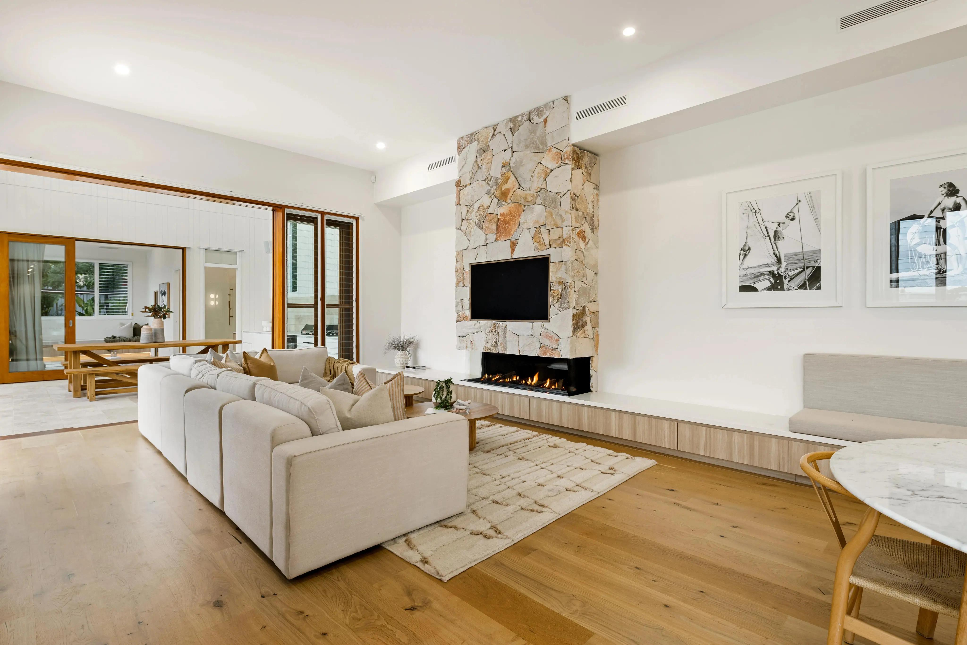 Architectural modern coastal interior design in a luxury home, featuring a massive natural stone fireplace, light wood flooring, and integrated joinery.