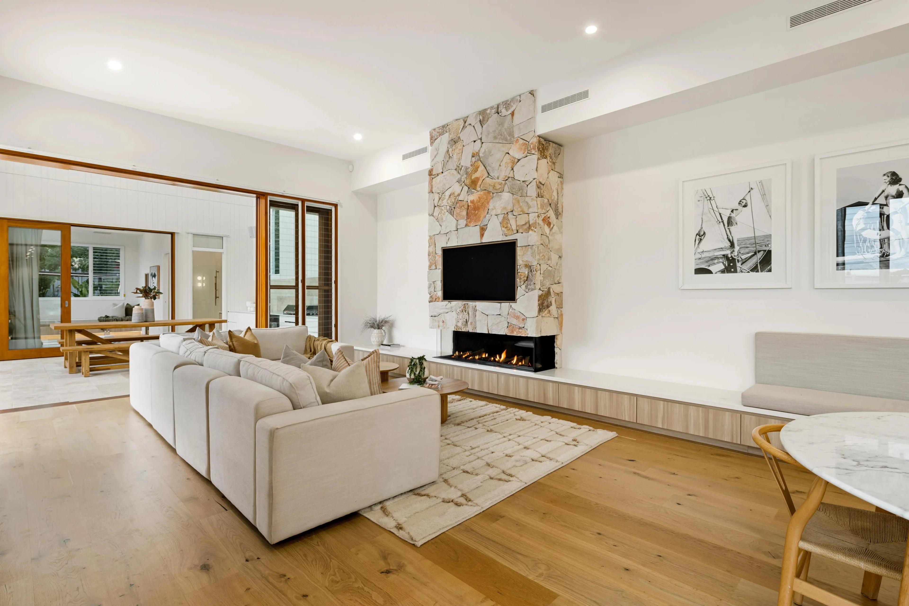 Architectural modern coastal interior design in a luxury home, featuring a massive natural stone fireplace, light wood flooring, and integrated joinery.