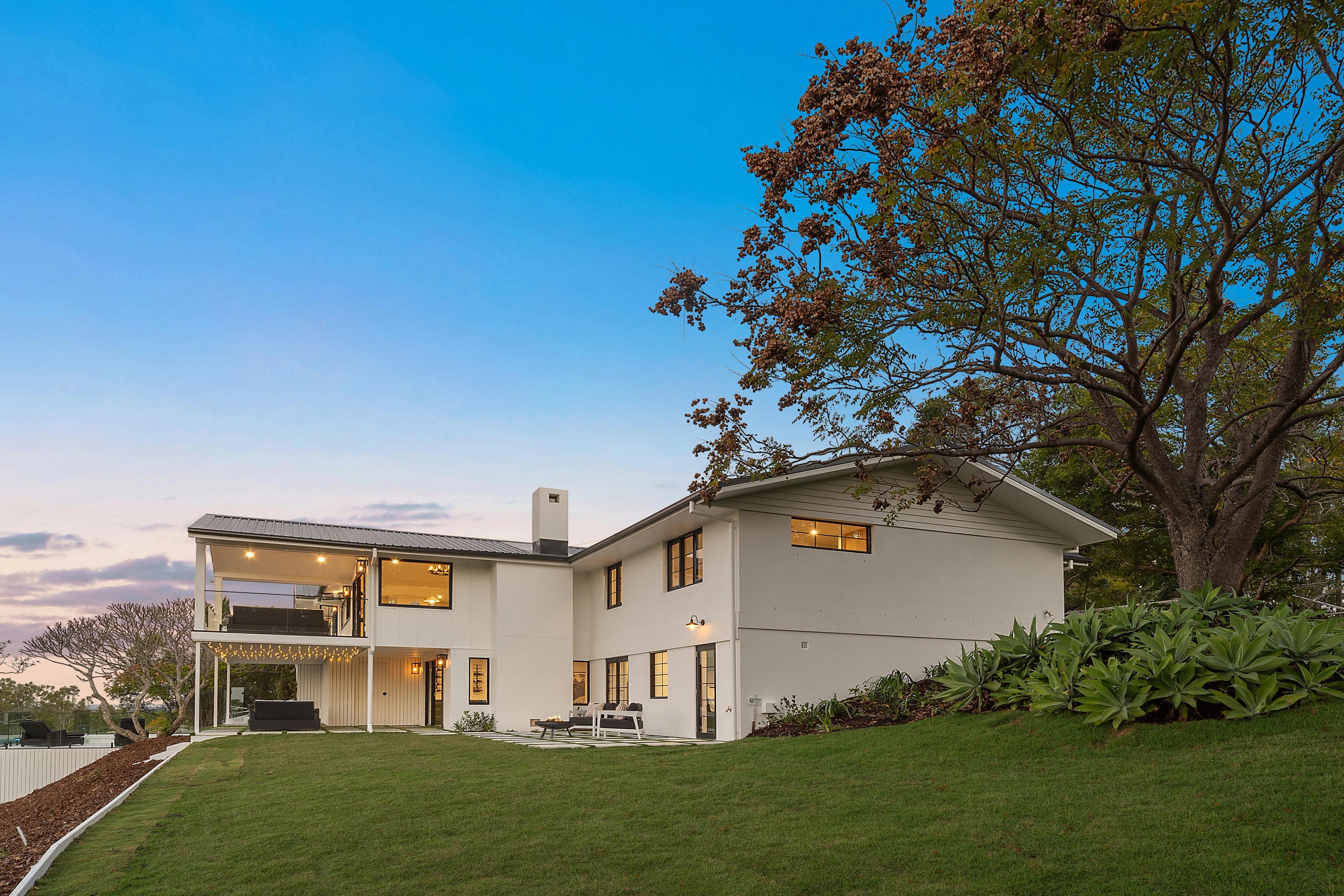 Two-storey rear elevation at dusk with upper covered deck, chimney and sloping lawn