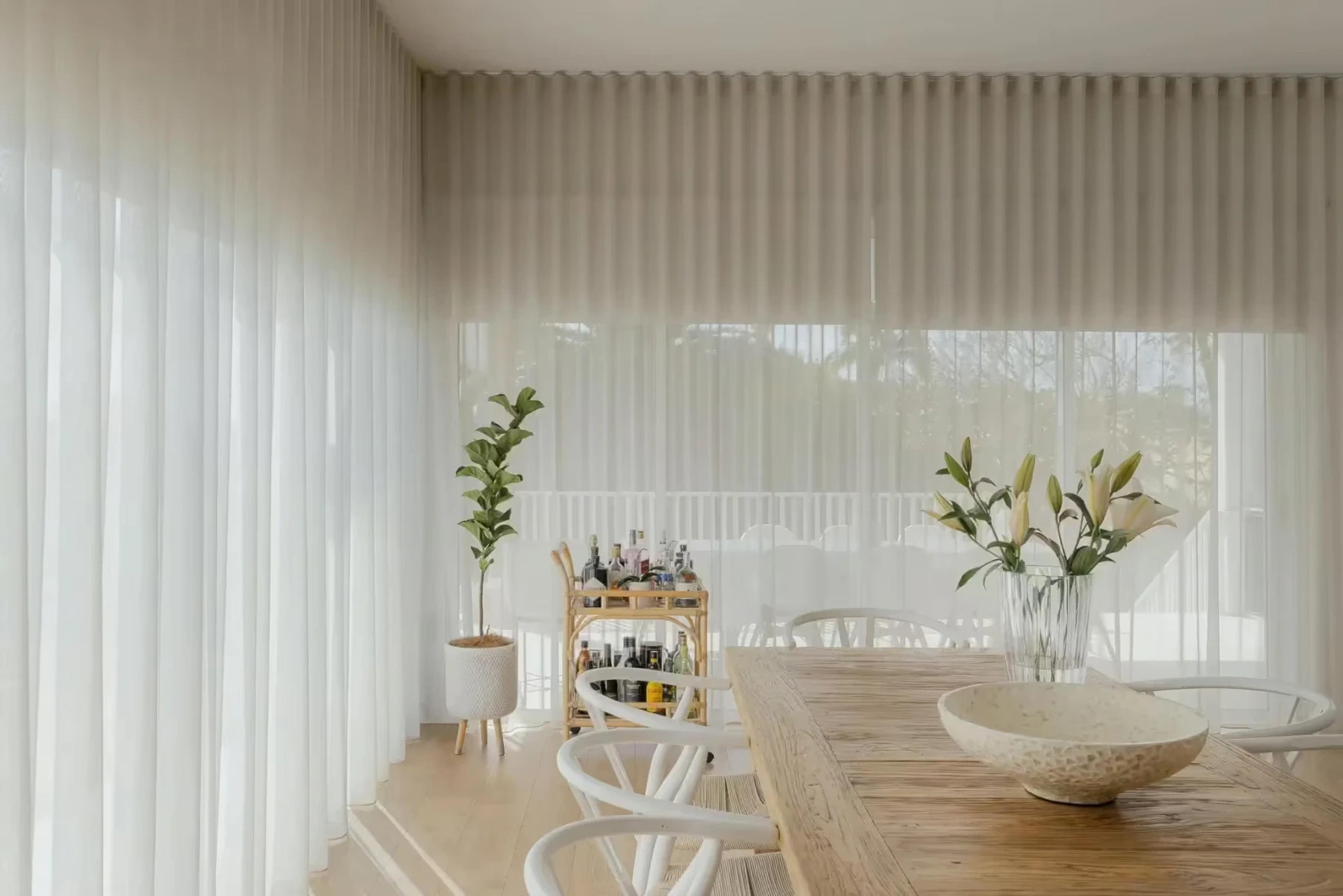 Timber dining table beside sheer curtains and bar cart