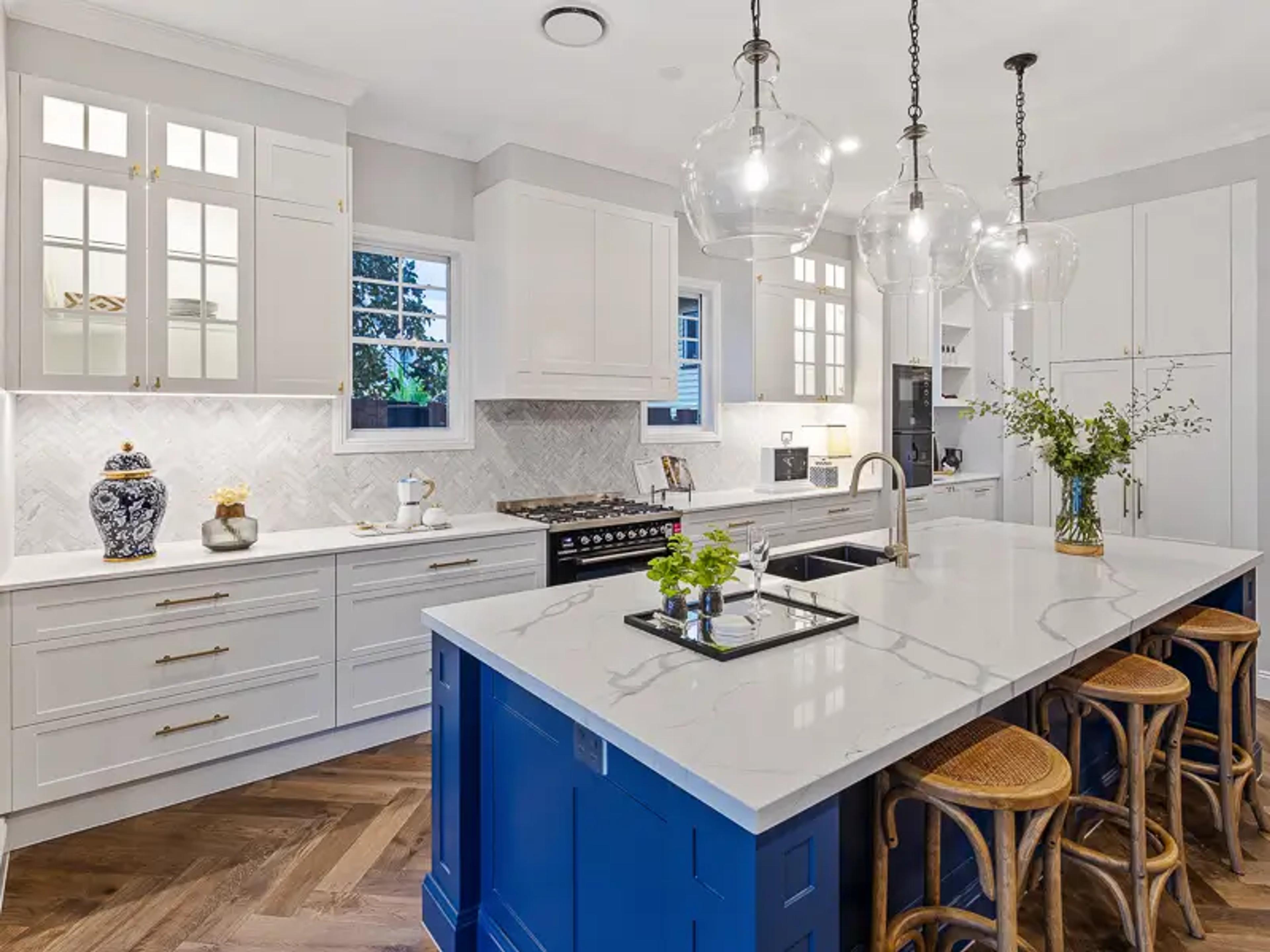 White kitchen with blue island, stone benchtop and pendant lights