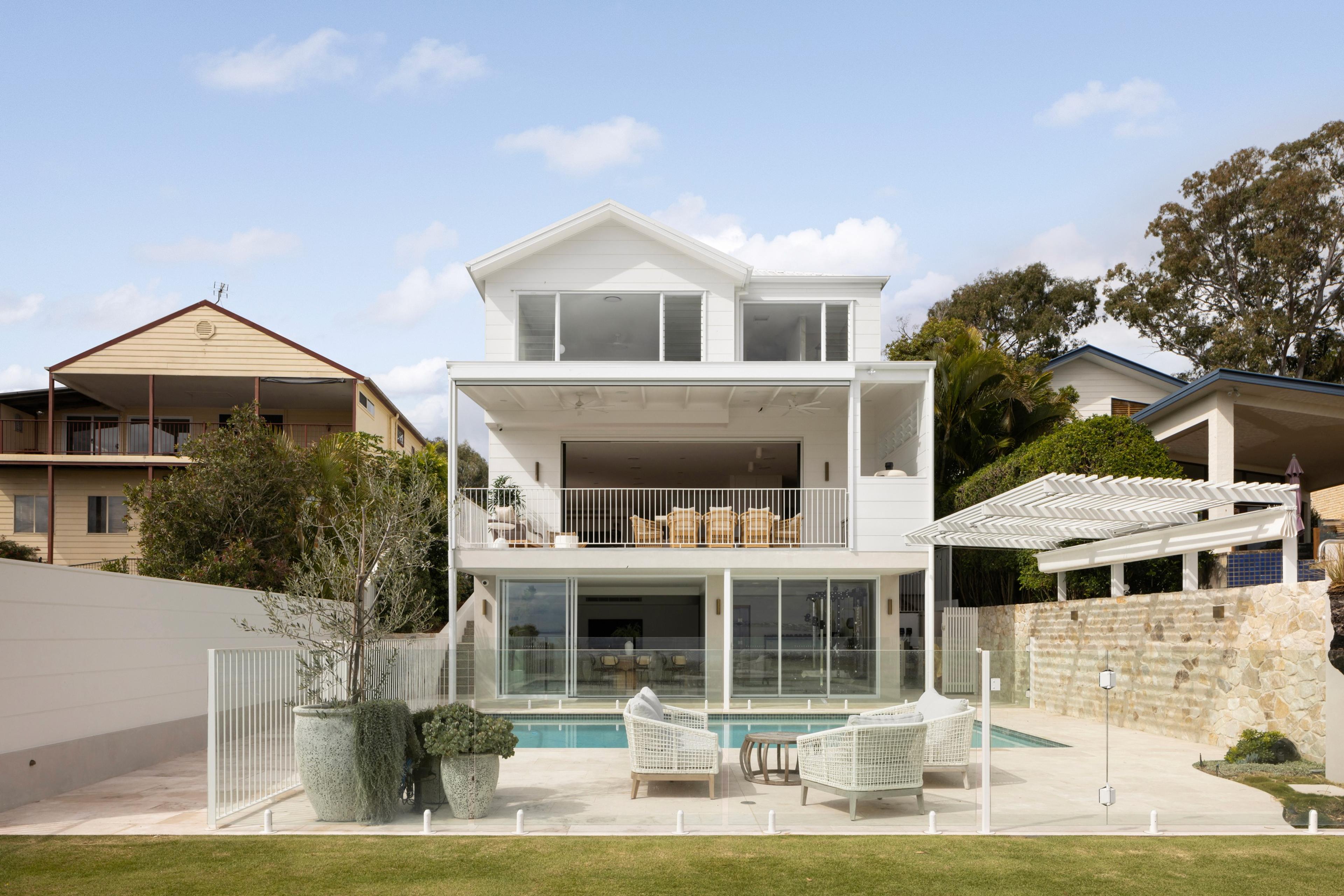 Rear elevation of white home above pool and garden