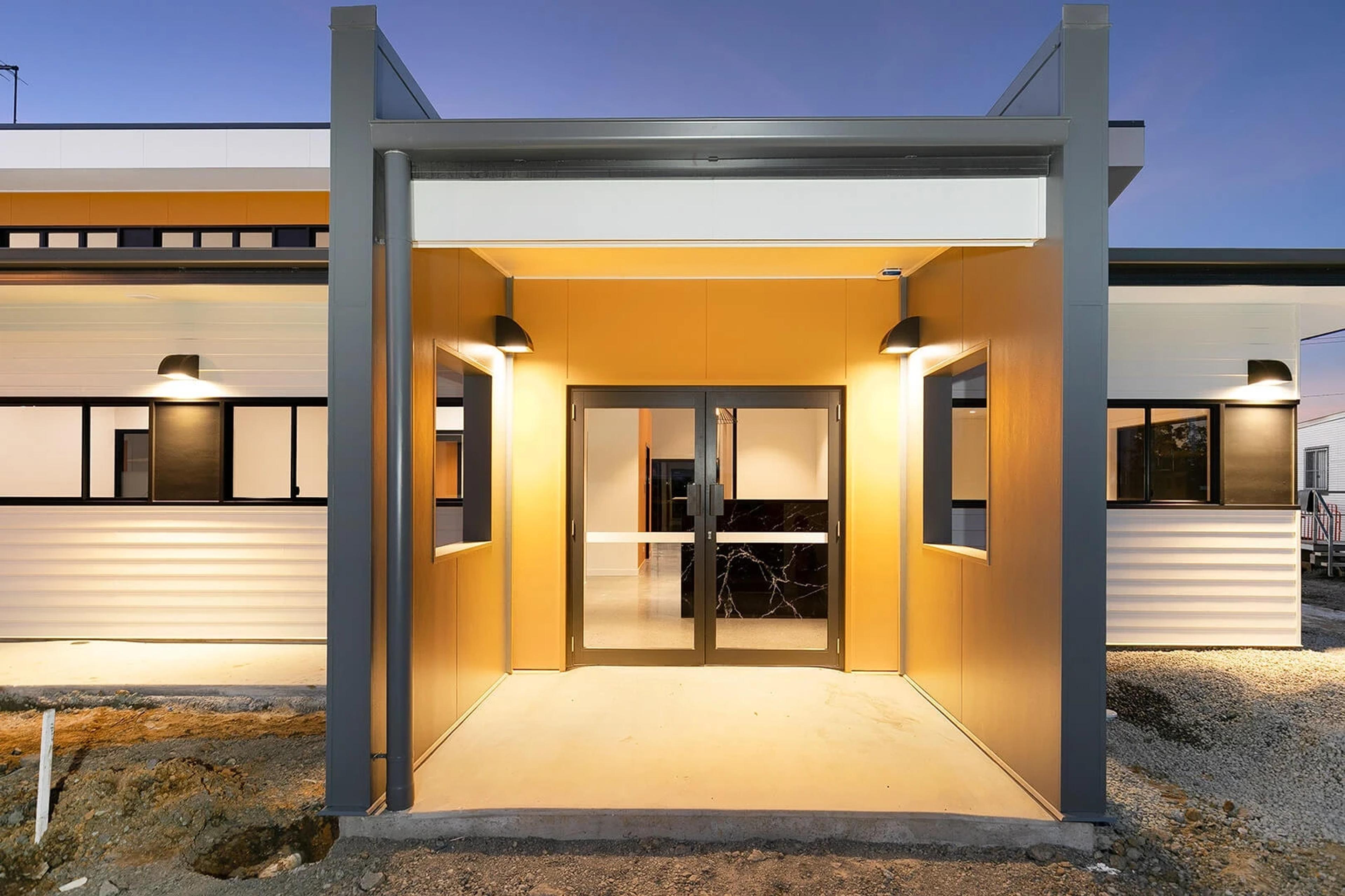 Front entrance with timber clad portal and glass doors at dusk