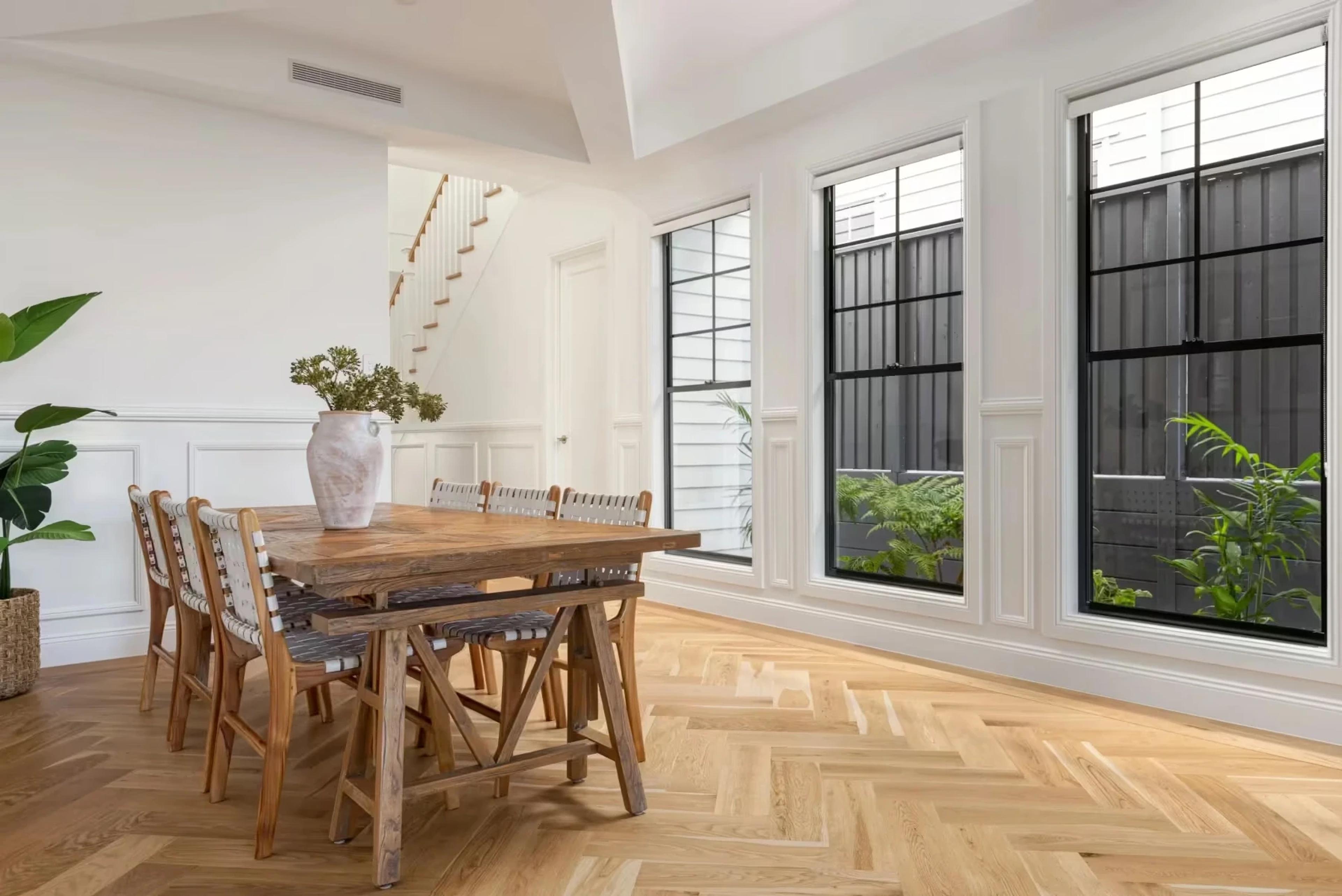 Dining area with timber table, staircase and tall black windows