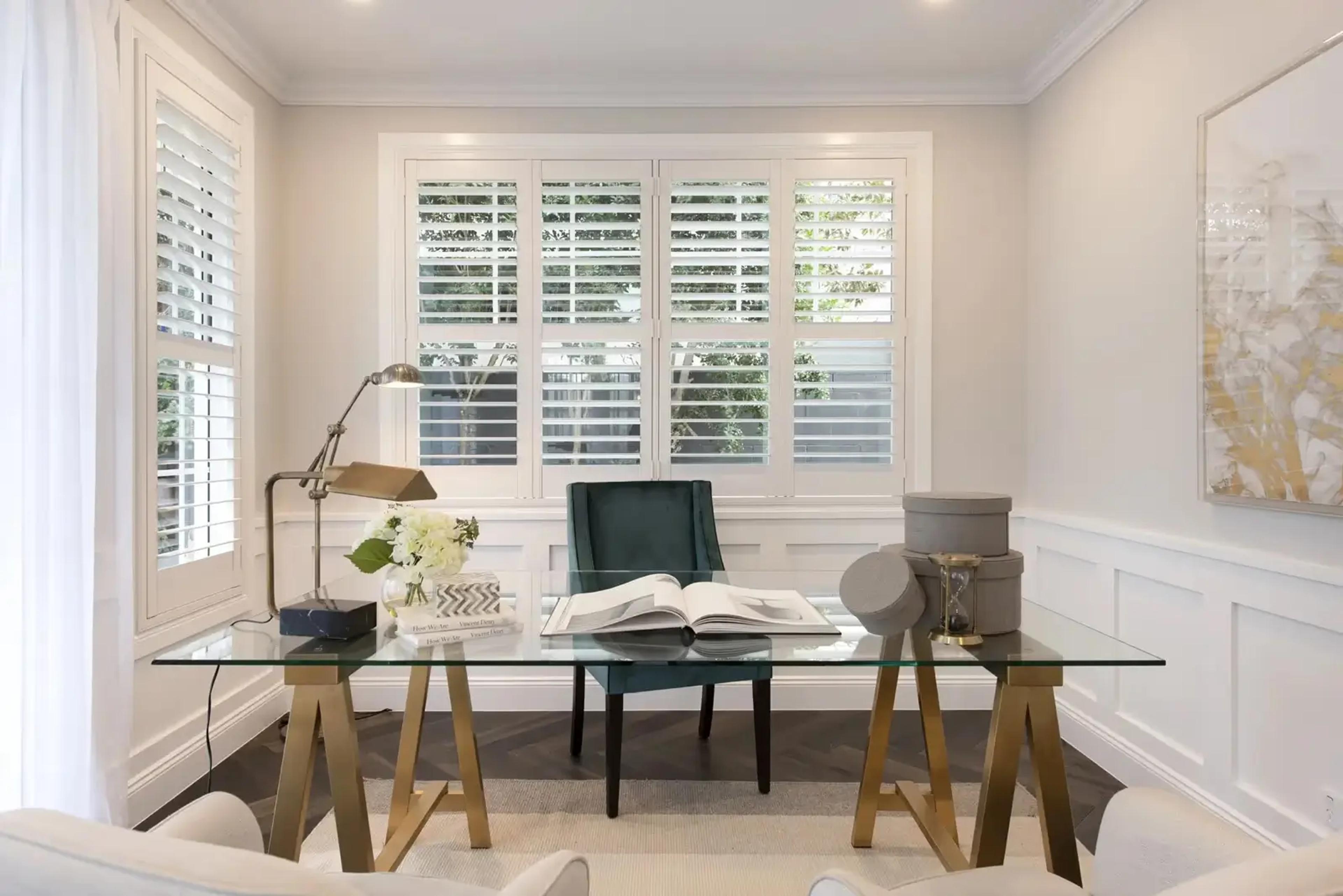 Home study with glass desk, plantation shutters and green chair