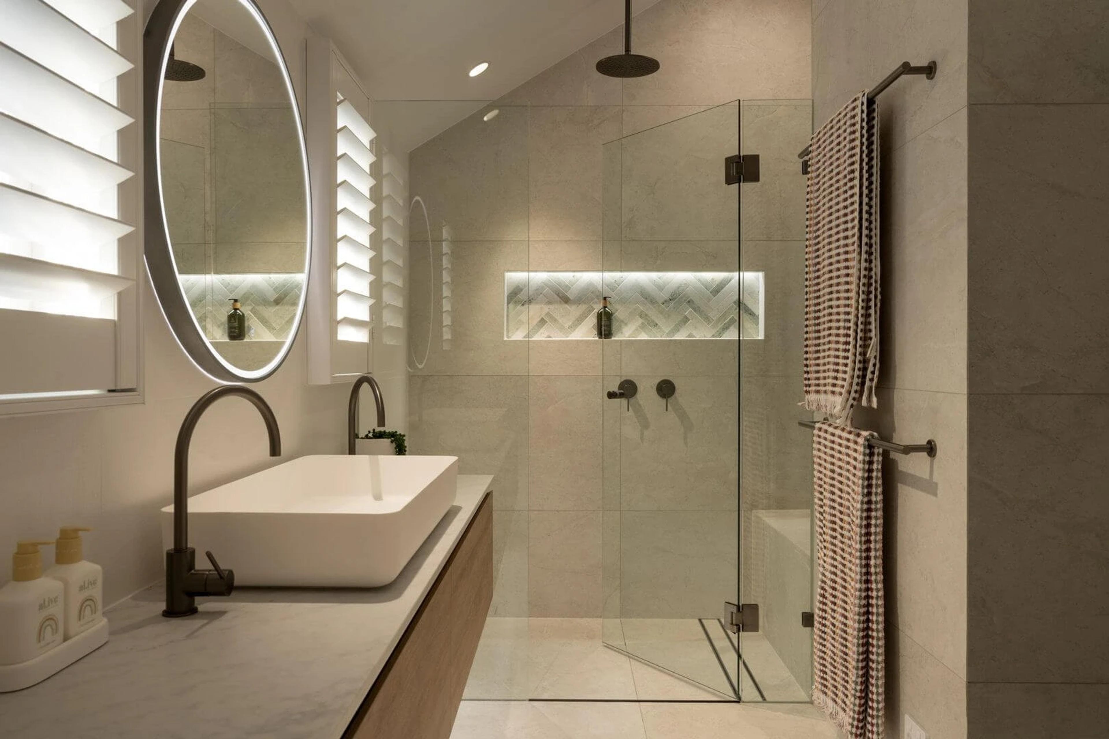 Bathroom with round mirror, black tapware and glass shower