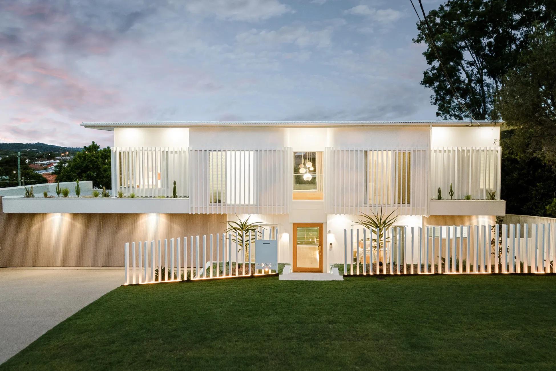 Street facing facade of white two storey home with timber entry door at dusk