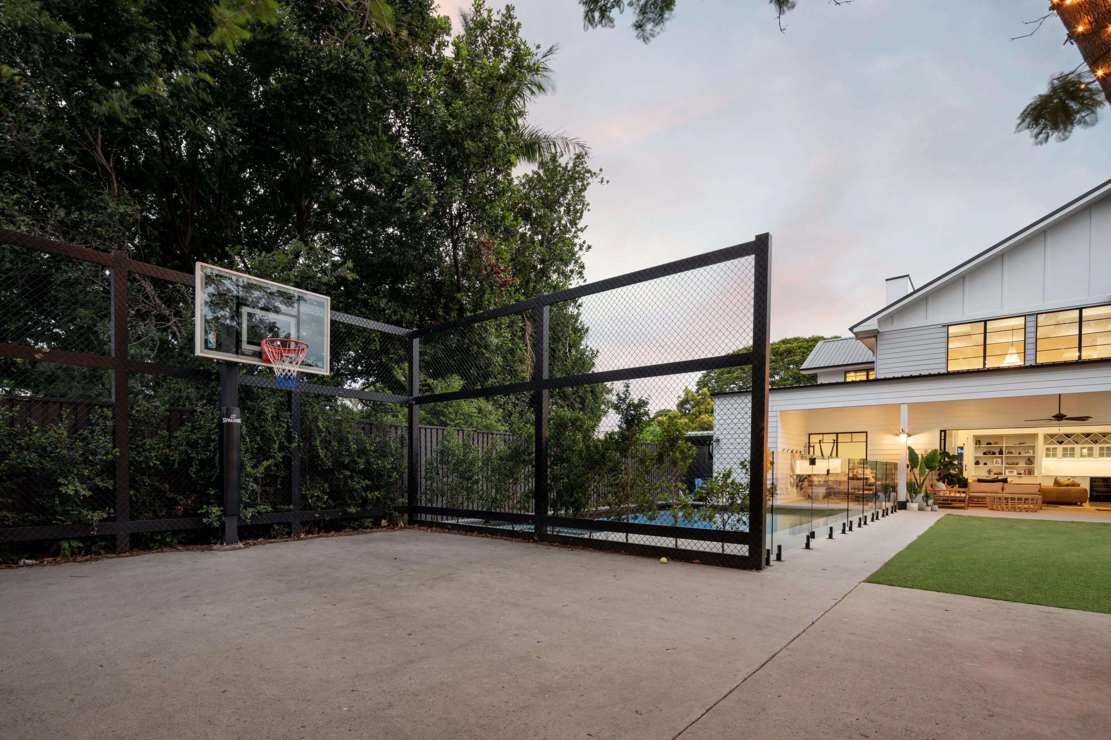 Backyard basketball court and pool beside the home at dusk