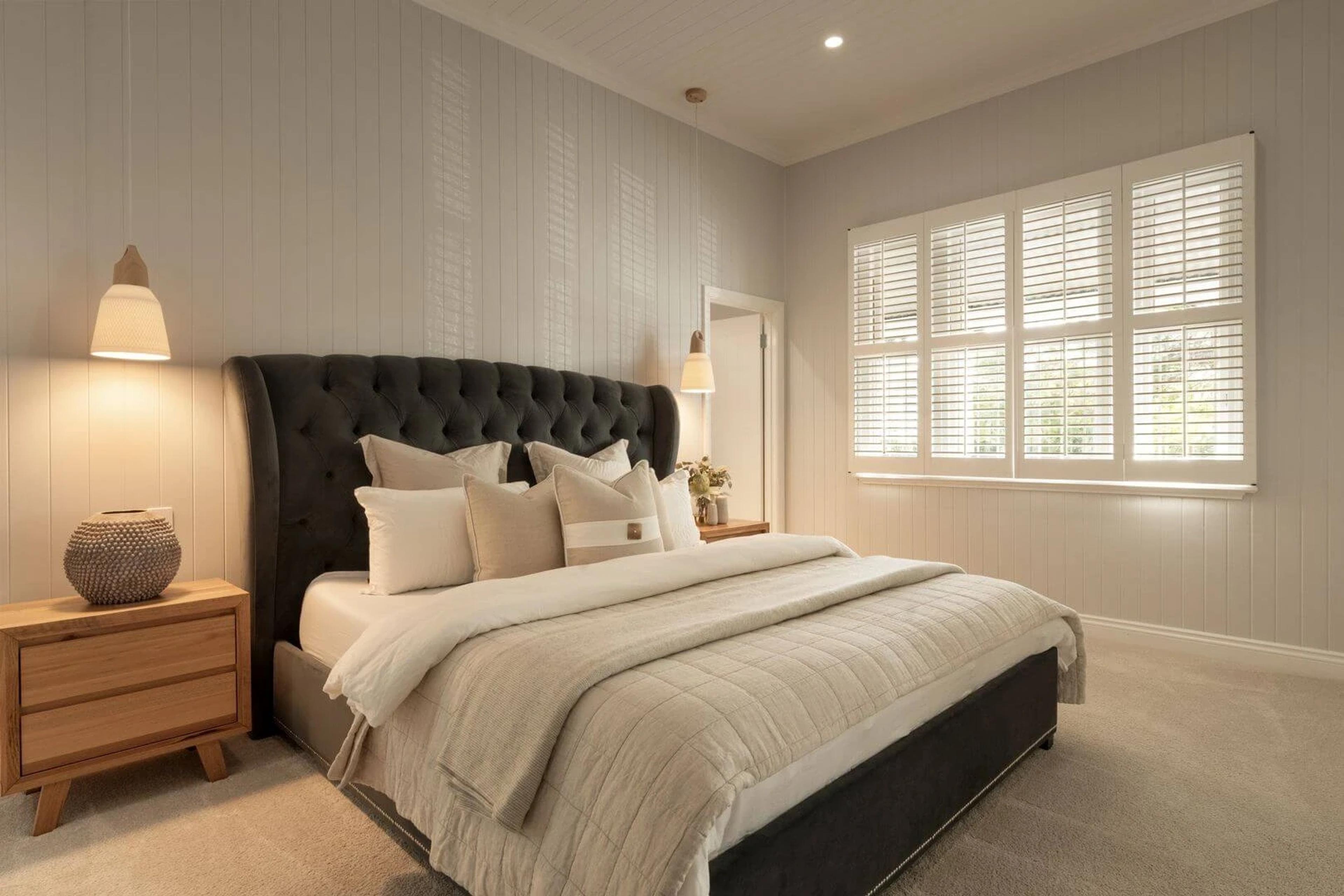 Main bedroom with tufted charcoal bedhead and plantation shutters
