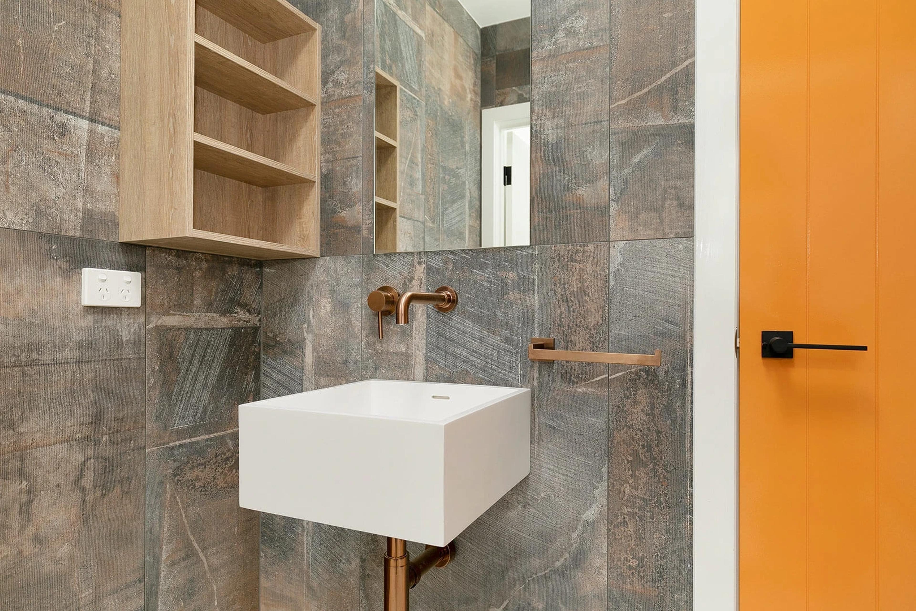 Bathroom with stone tiles, wall basin and orange door
