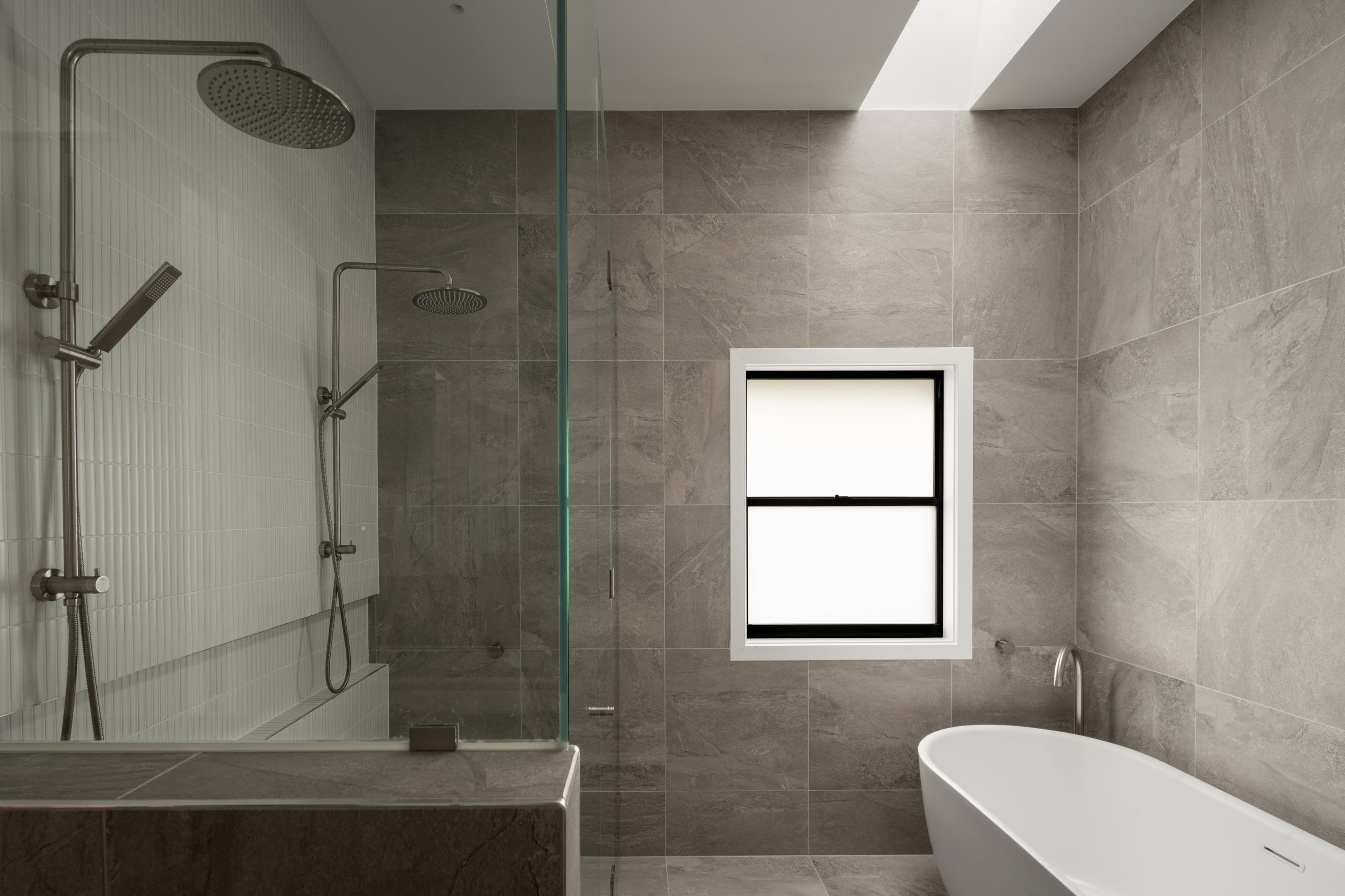 Grey tiled bathroom with twin showers and freestanding bath