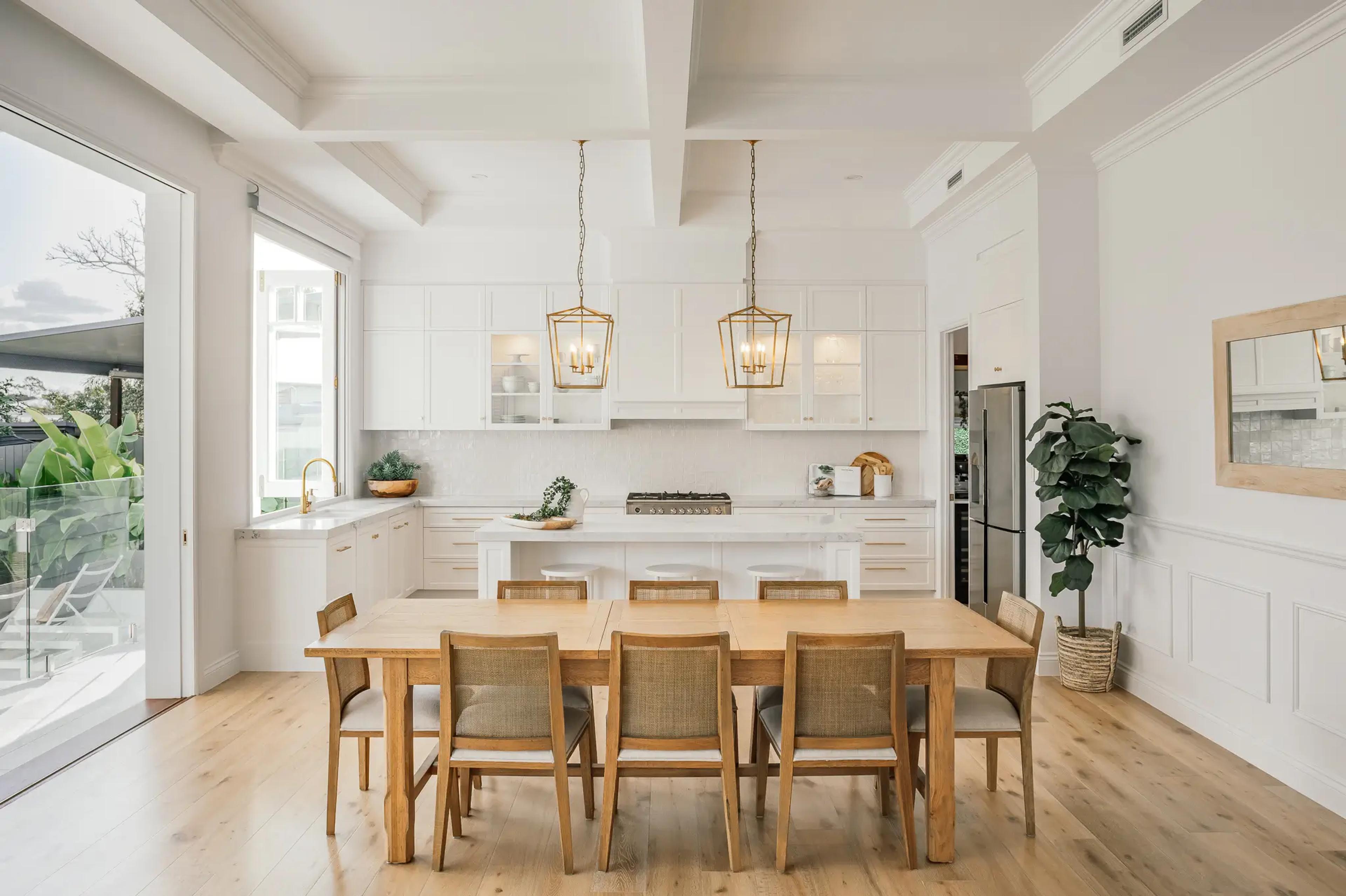 White kitchen with island, pendant lights and timber dining table