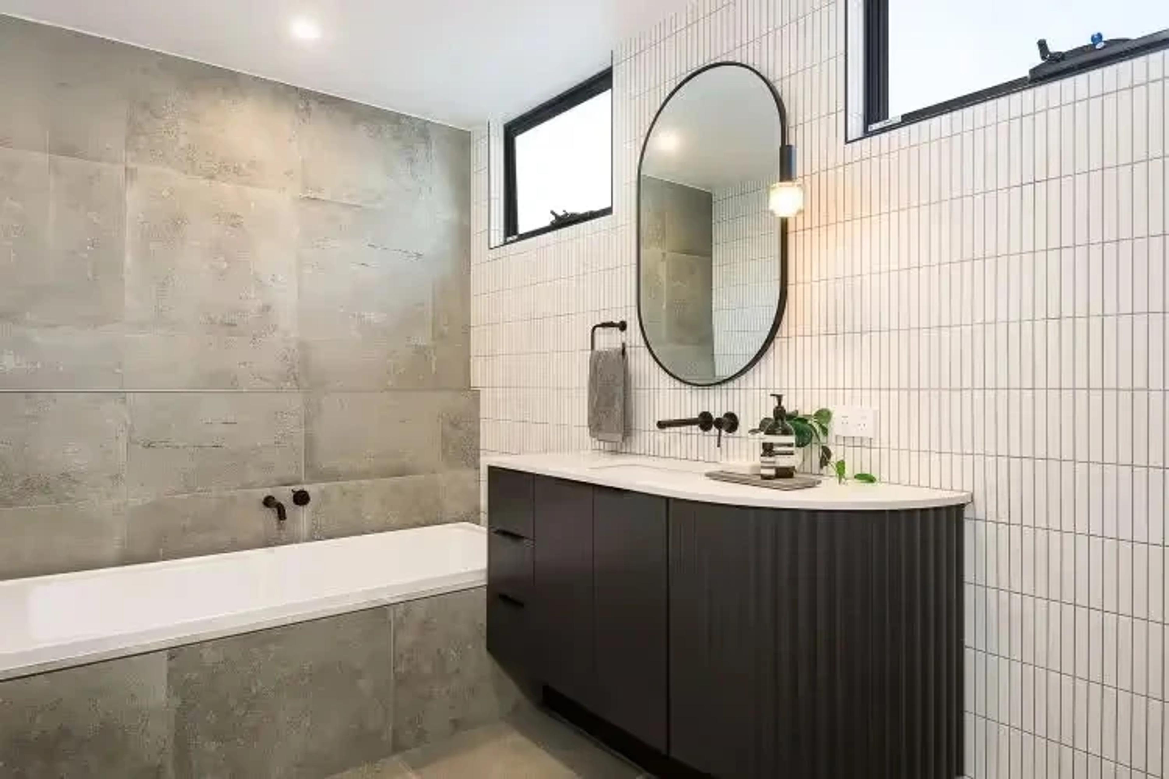 Bathroom with dark vanity, oval mirror and concrete tiling