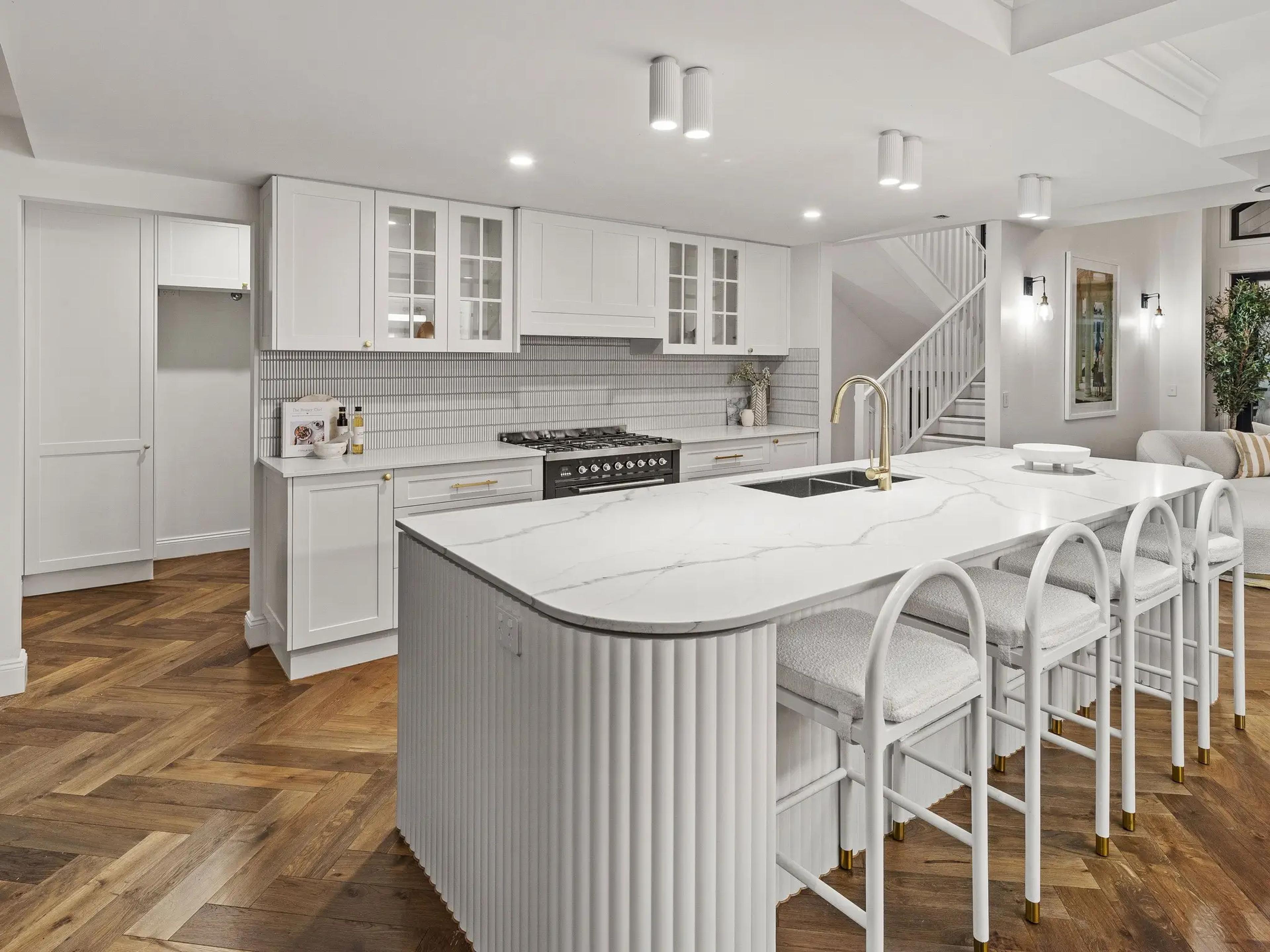 White kitchen with stone island bench and bar stools