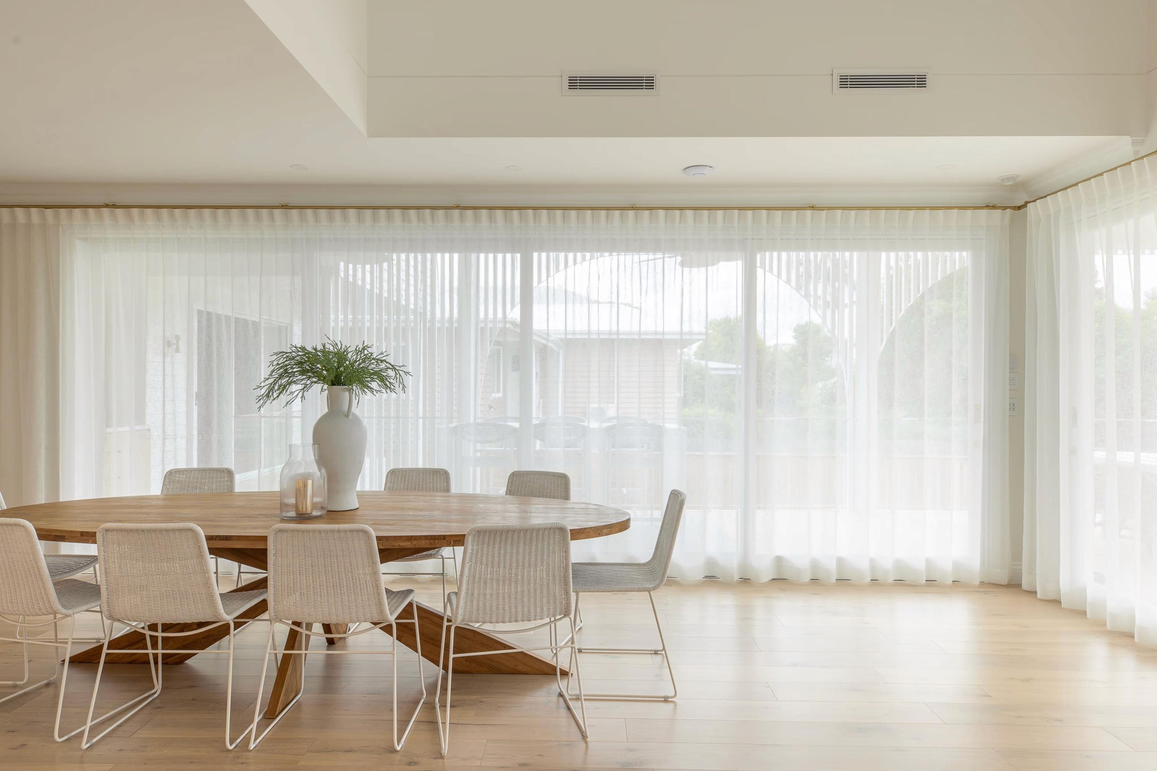Round timber dining table and chairs beside sheer curtained windows