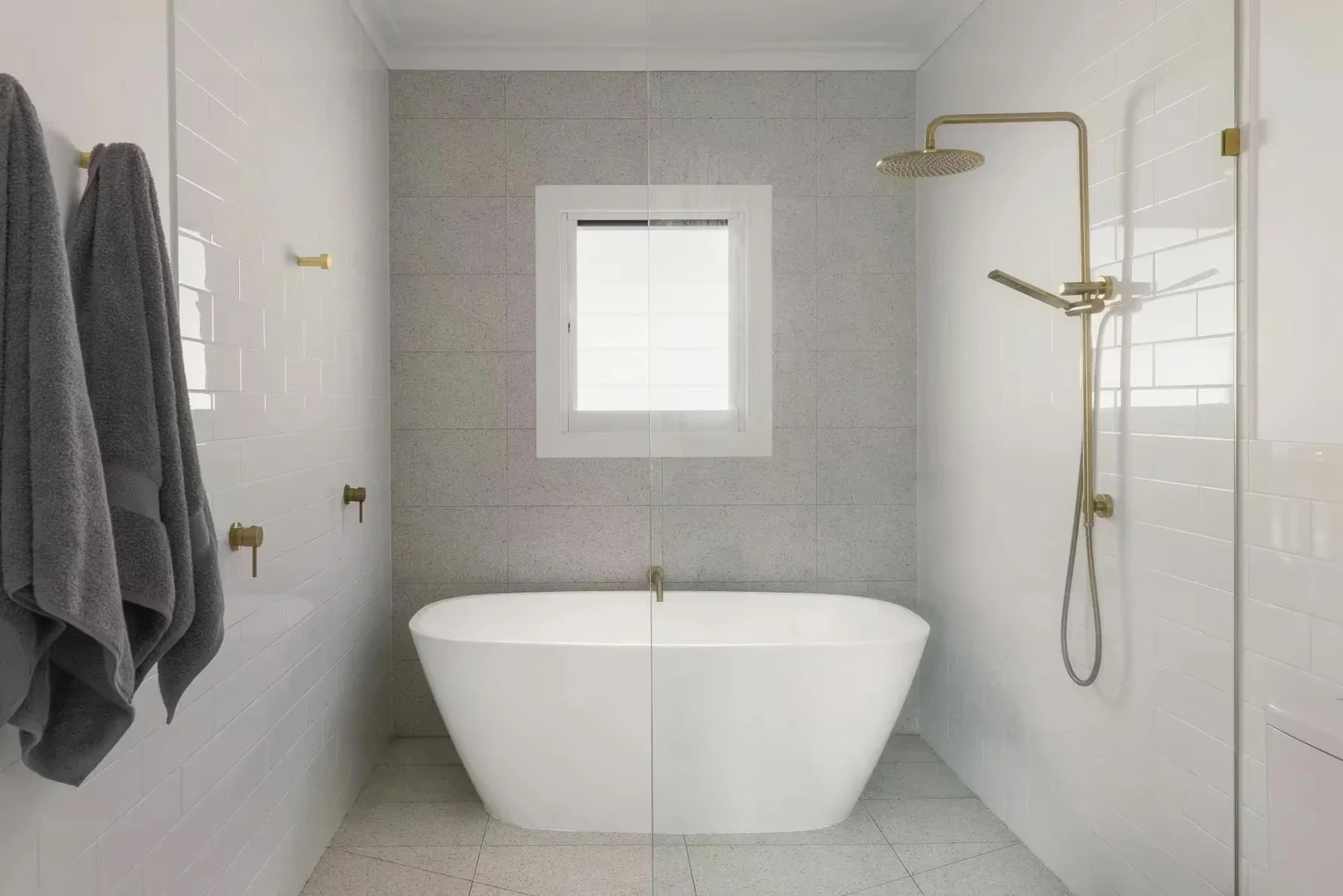 White tiled bathroom with freestanding bath and brass shower