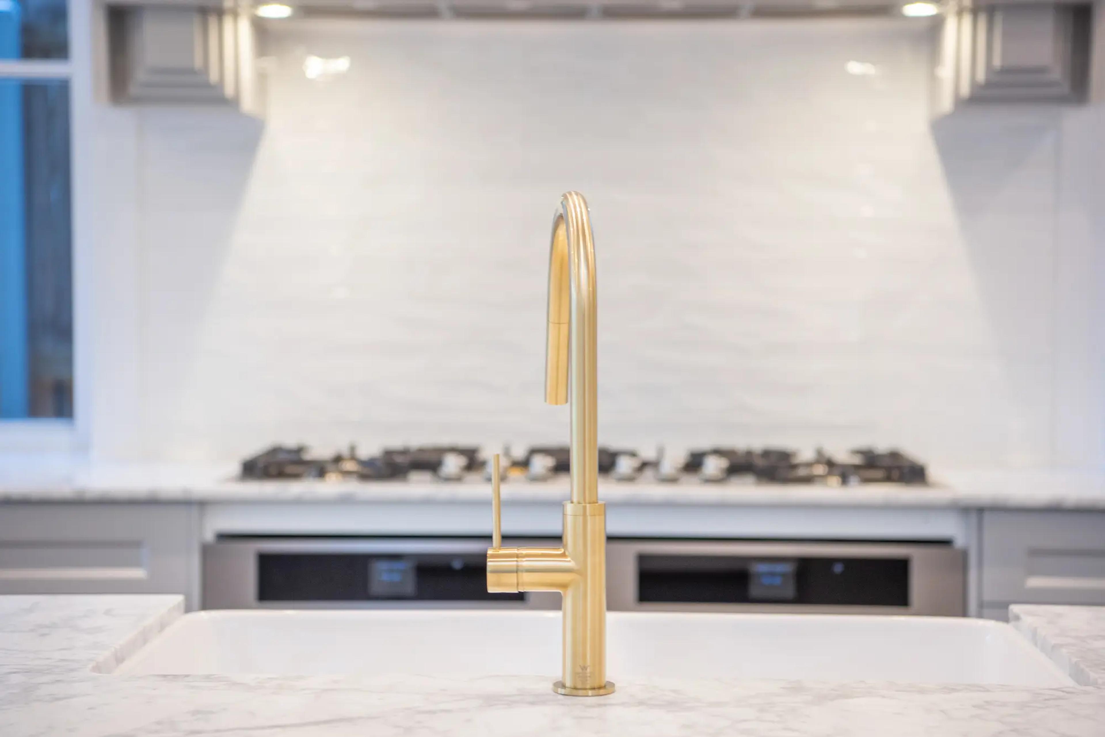 Brass kitchen tap over marble island near gas cooktop