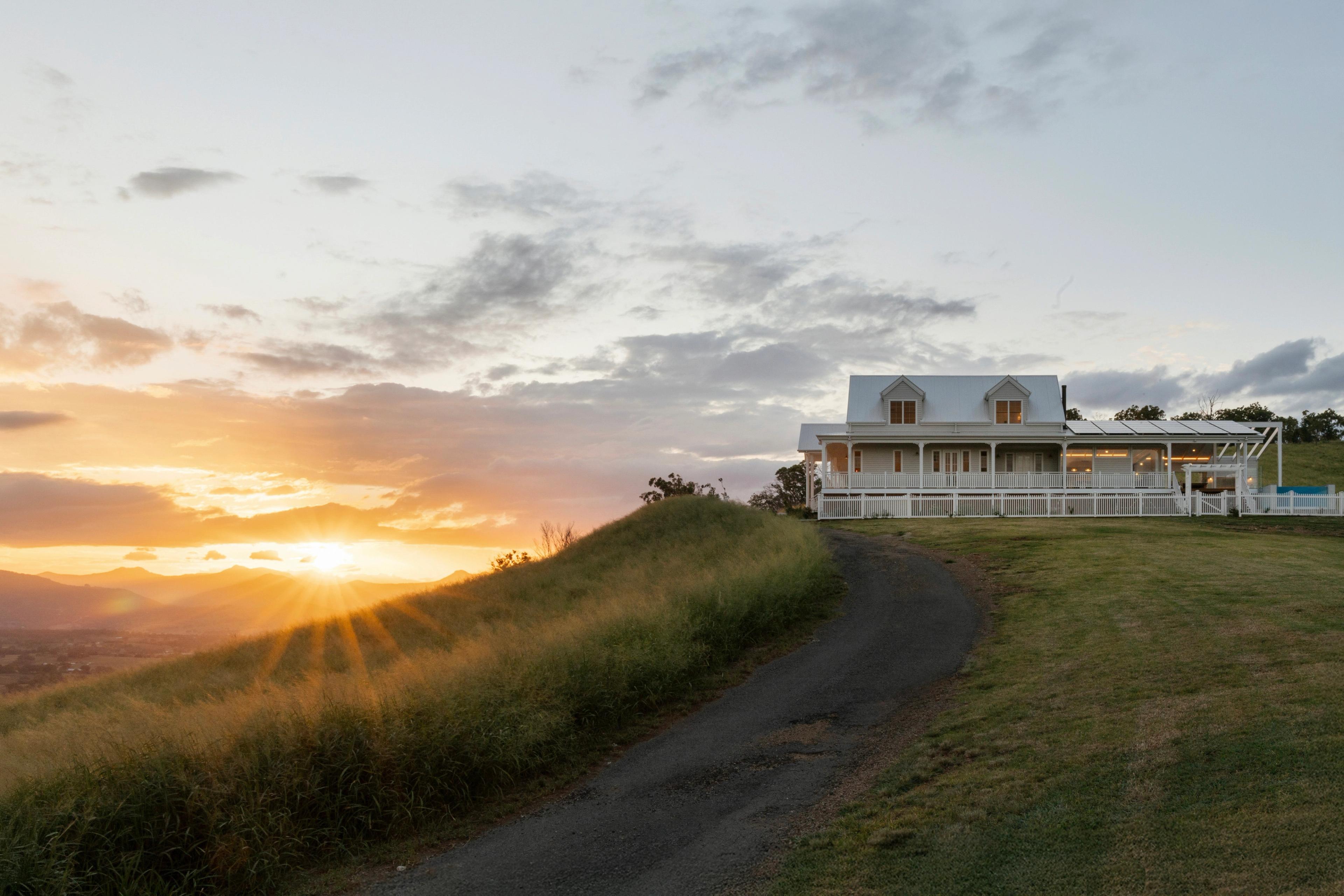 Homestead on hilltop at sunset with driveway and mountains