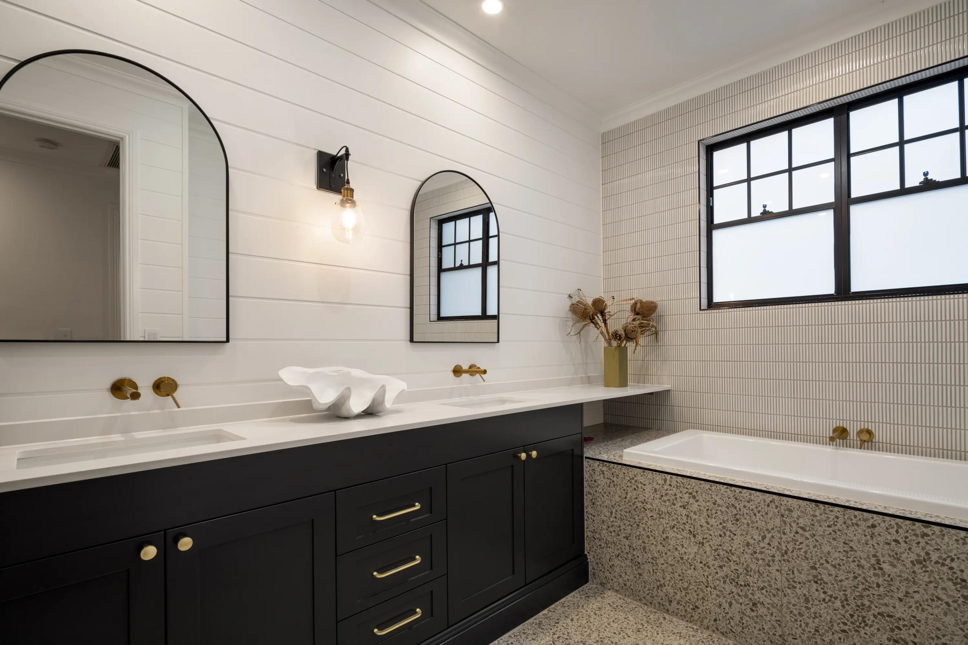 Bathroom with black double vanity, arched mirrors and terrazzo bathtub