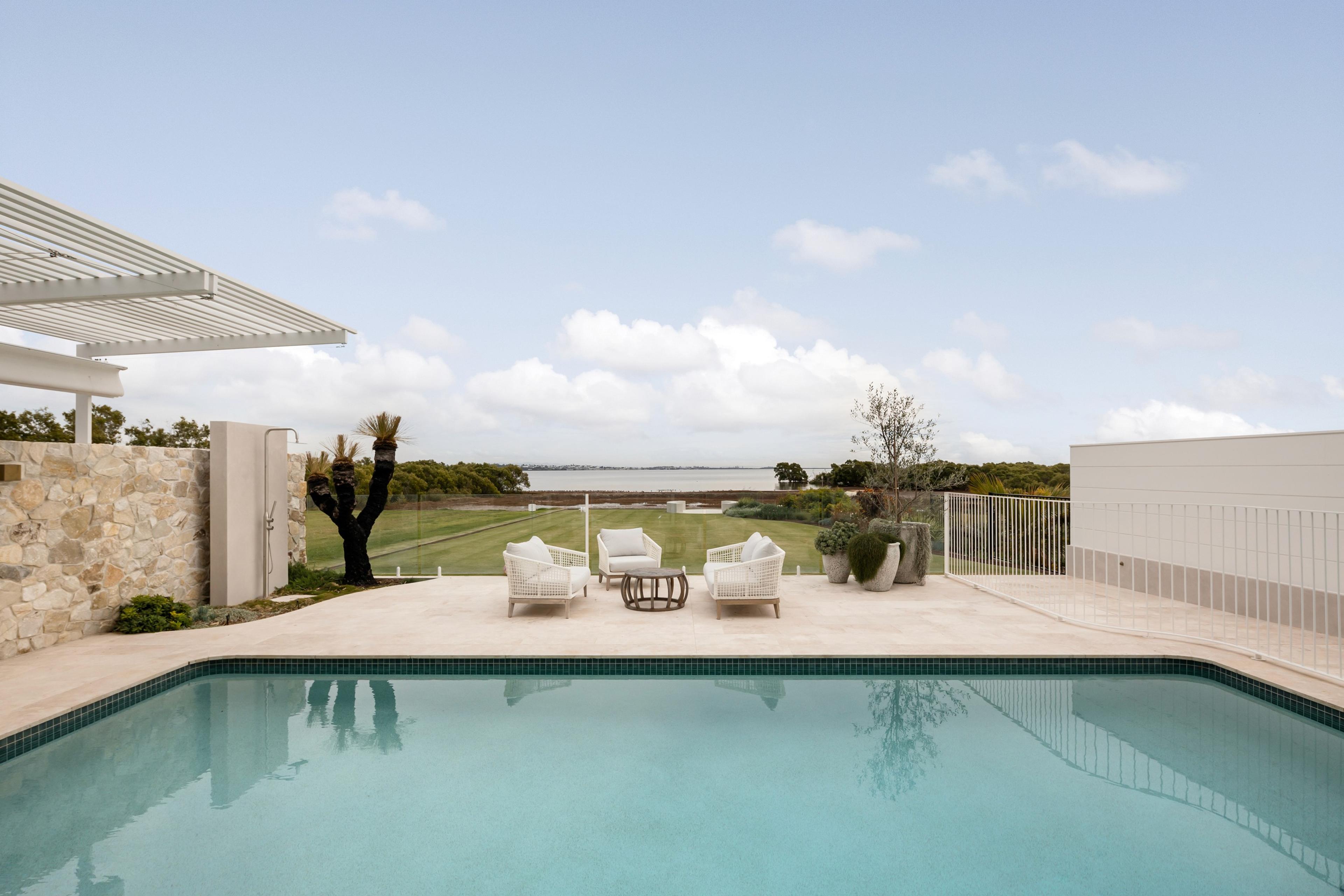 Pool terrace with lounge chairs overlooking grassy bay view