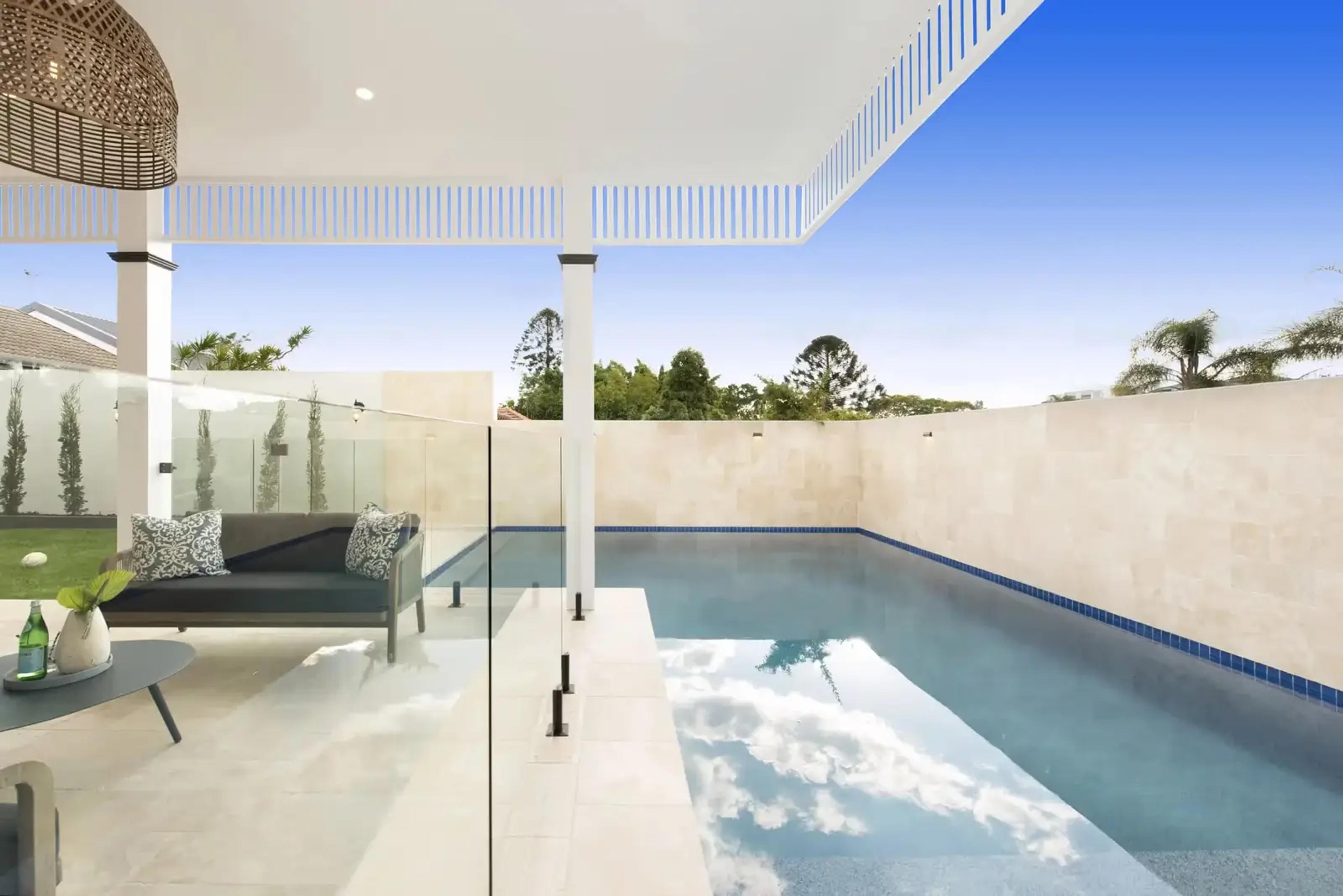 Swimming pool with glass fencing, stone wall and covered patio