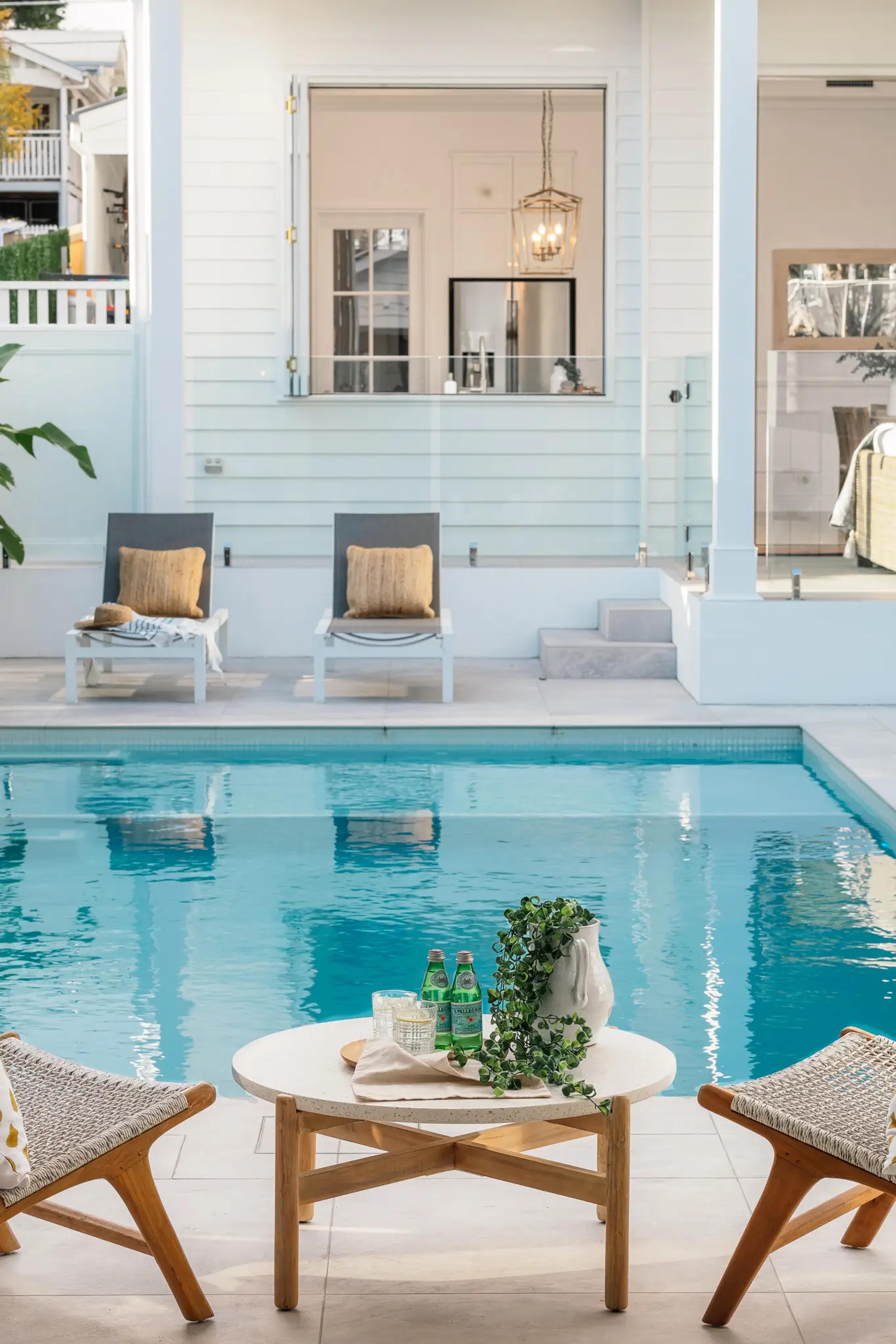 Swimming pool with sun loungers beside pale weatherboard home