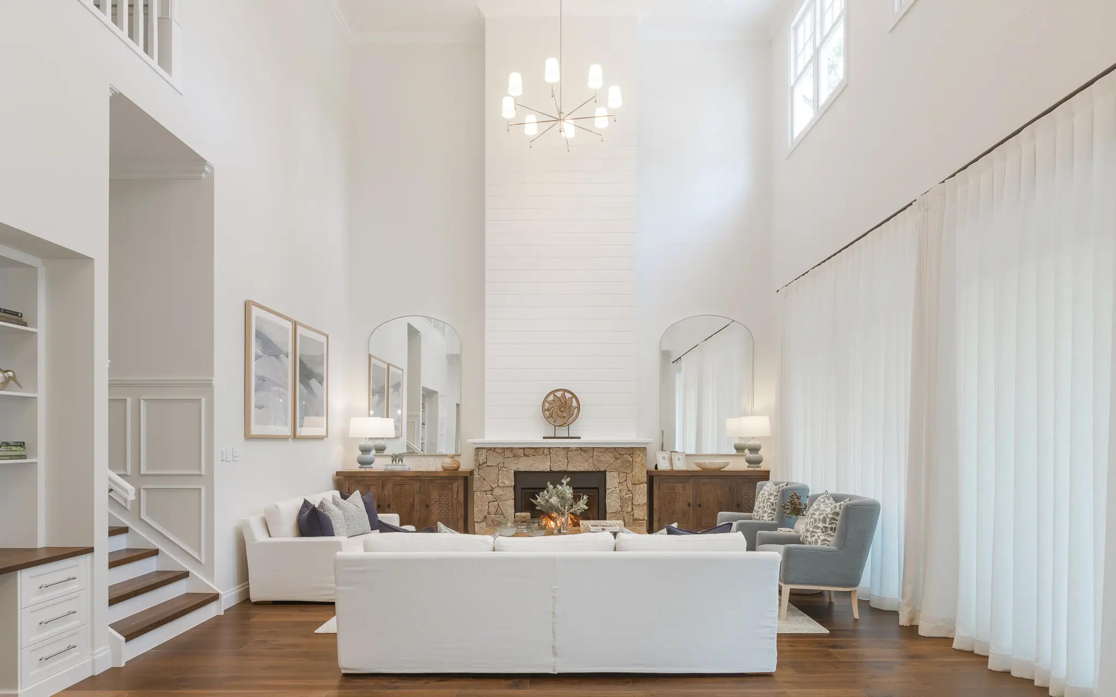 Soaring white living room with shiplap fireplace, arched mirrors and timber floors