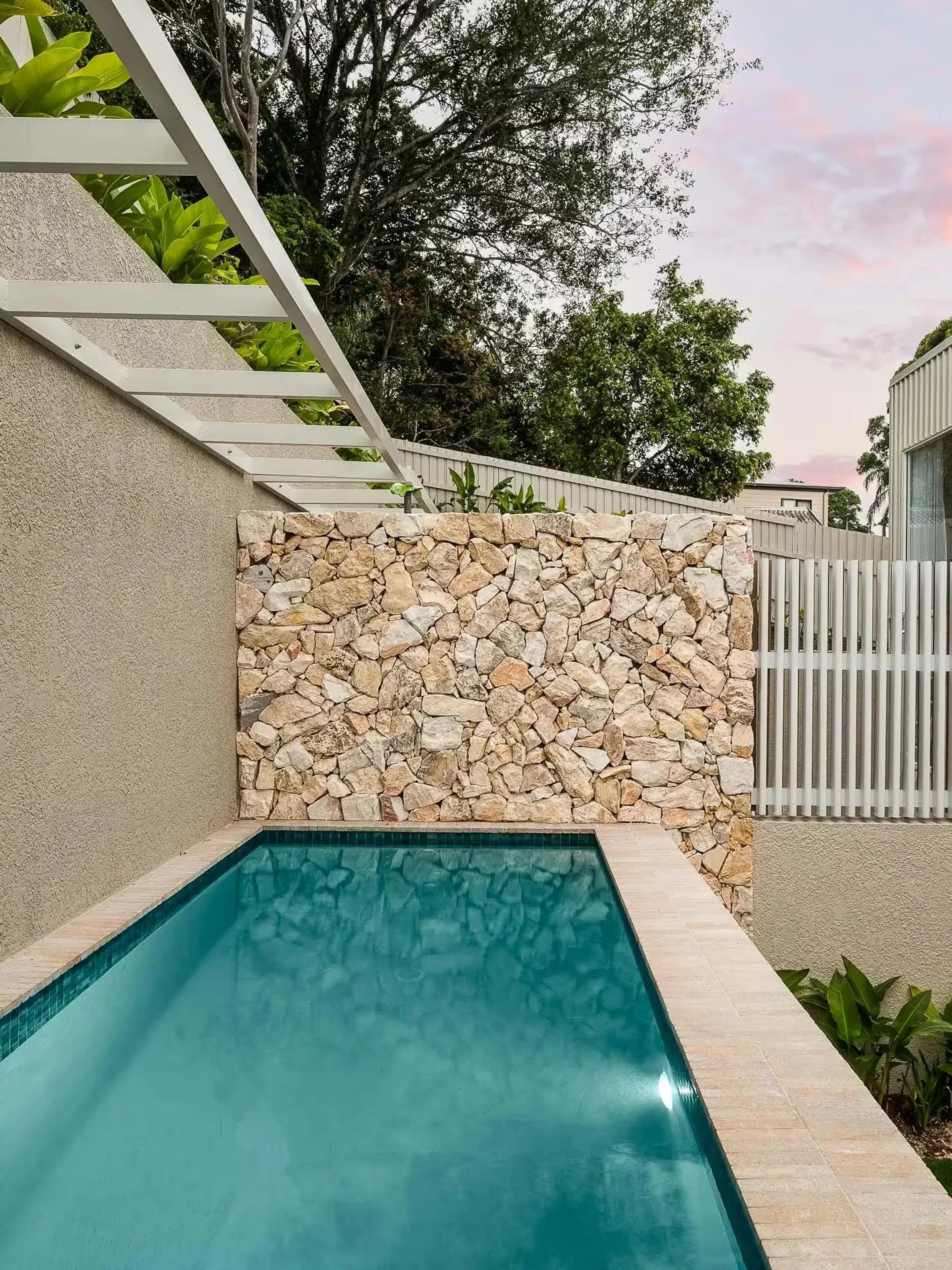 Narrow lap pool beside sandstone garden wall