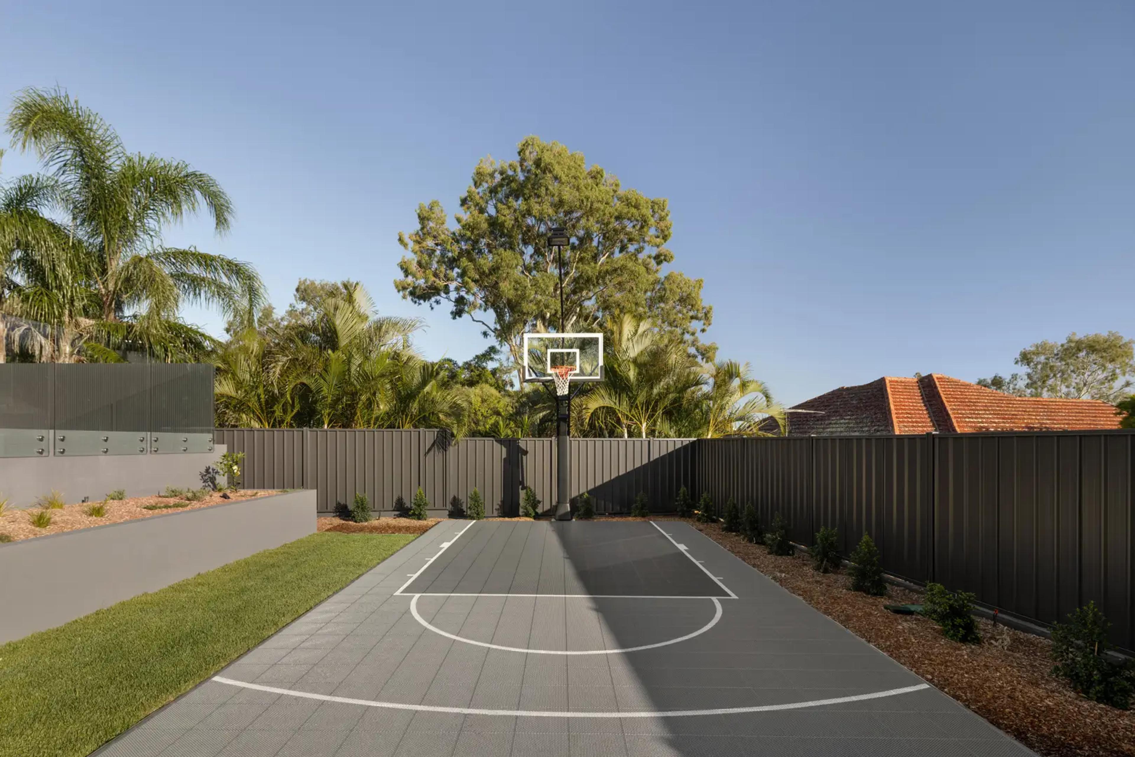 Landscaped backyard with basketball half court and fence