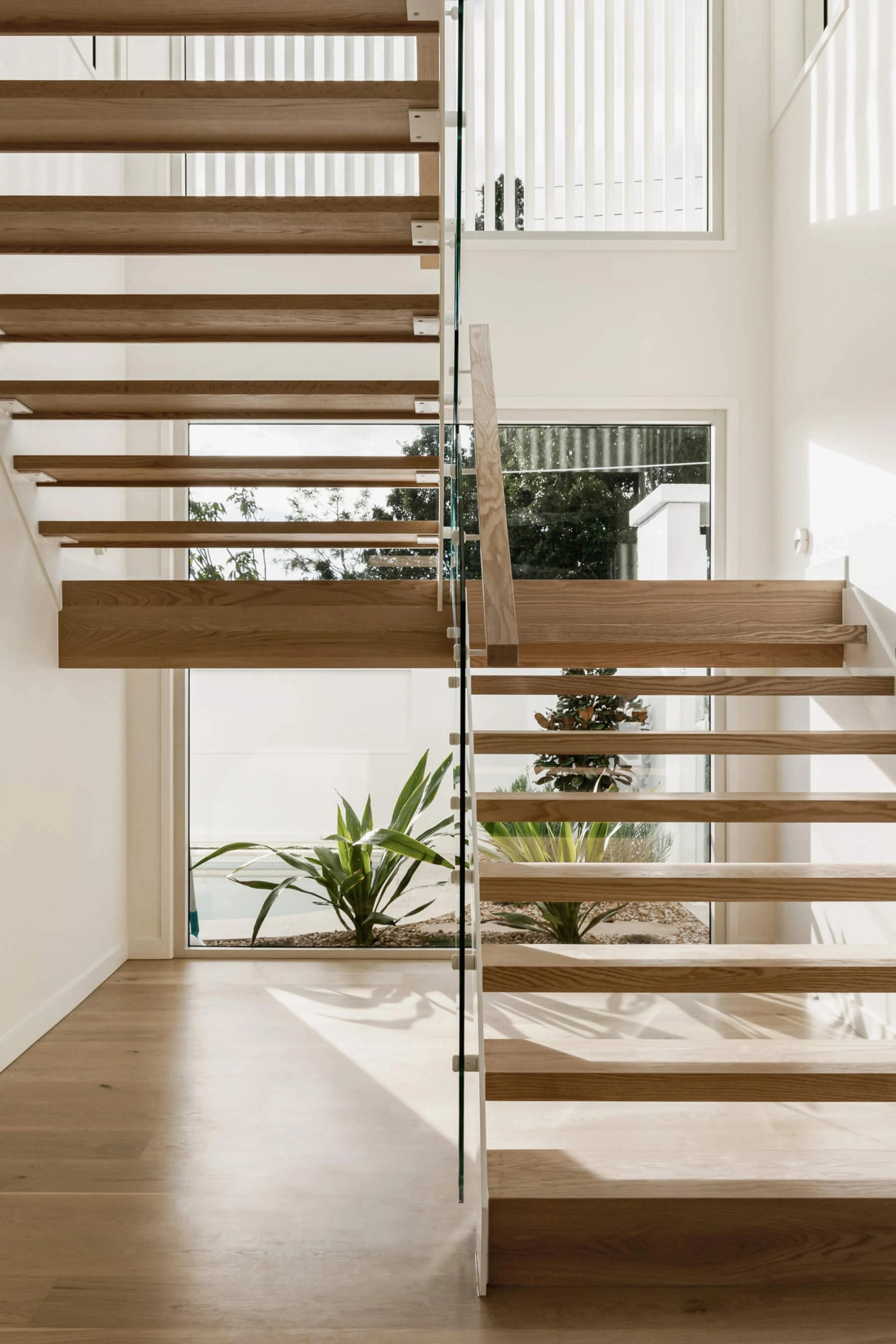 Floating timber staircase with glass balustrade and courtyard planting