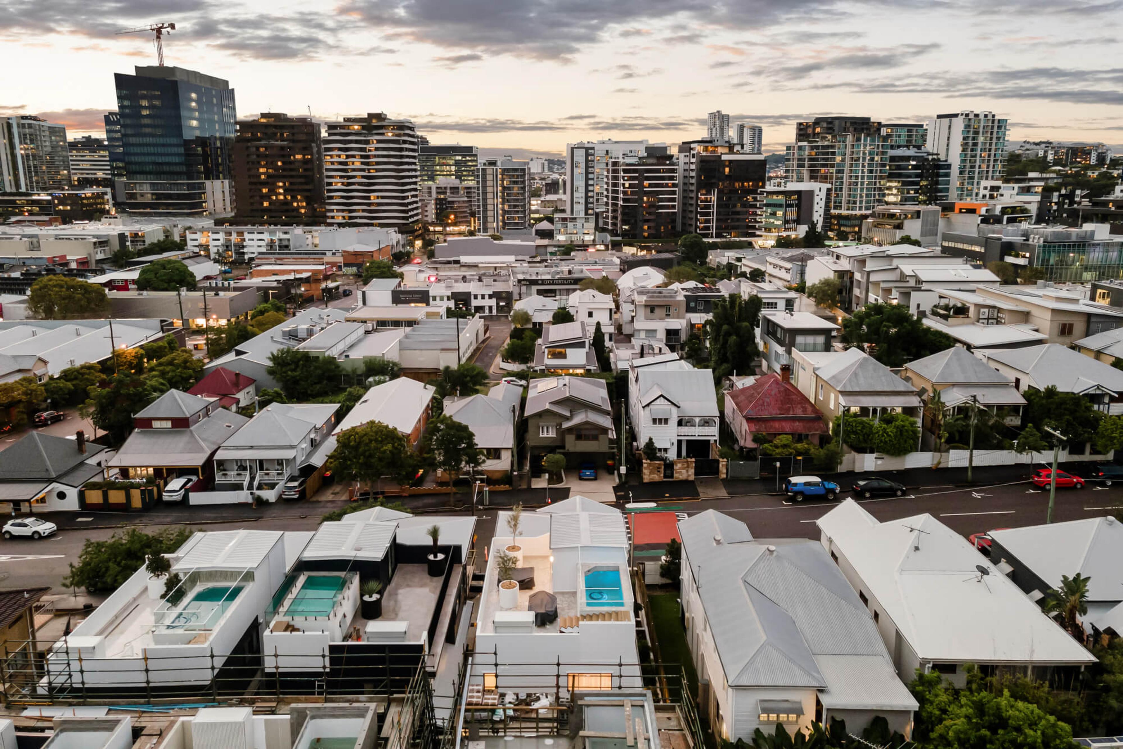 Aerial view of townhouses among suburban rooftops near a city skyline