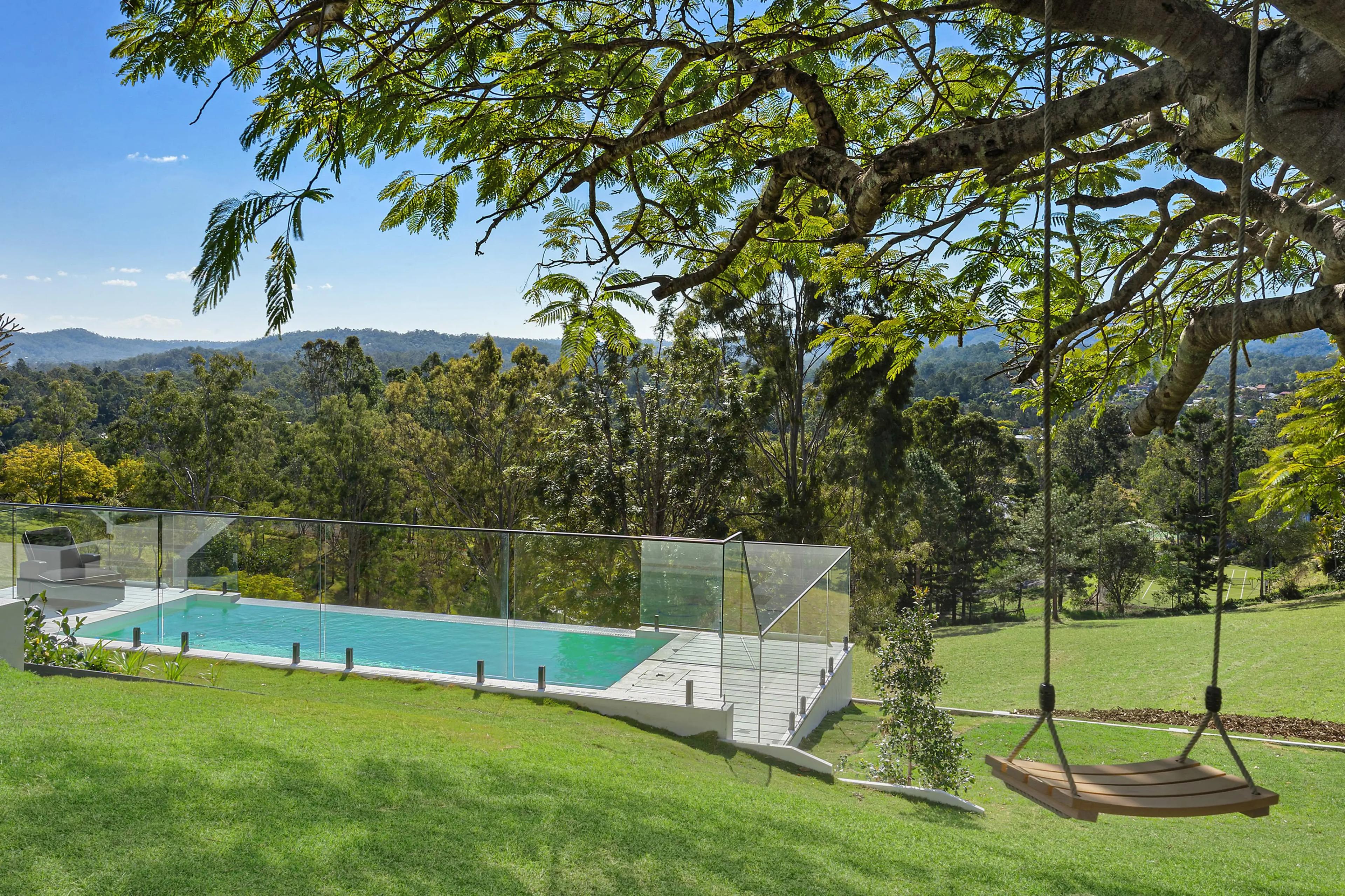 Sloping backyard with swimming pool, glass fencing and timber swing.