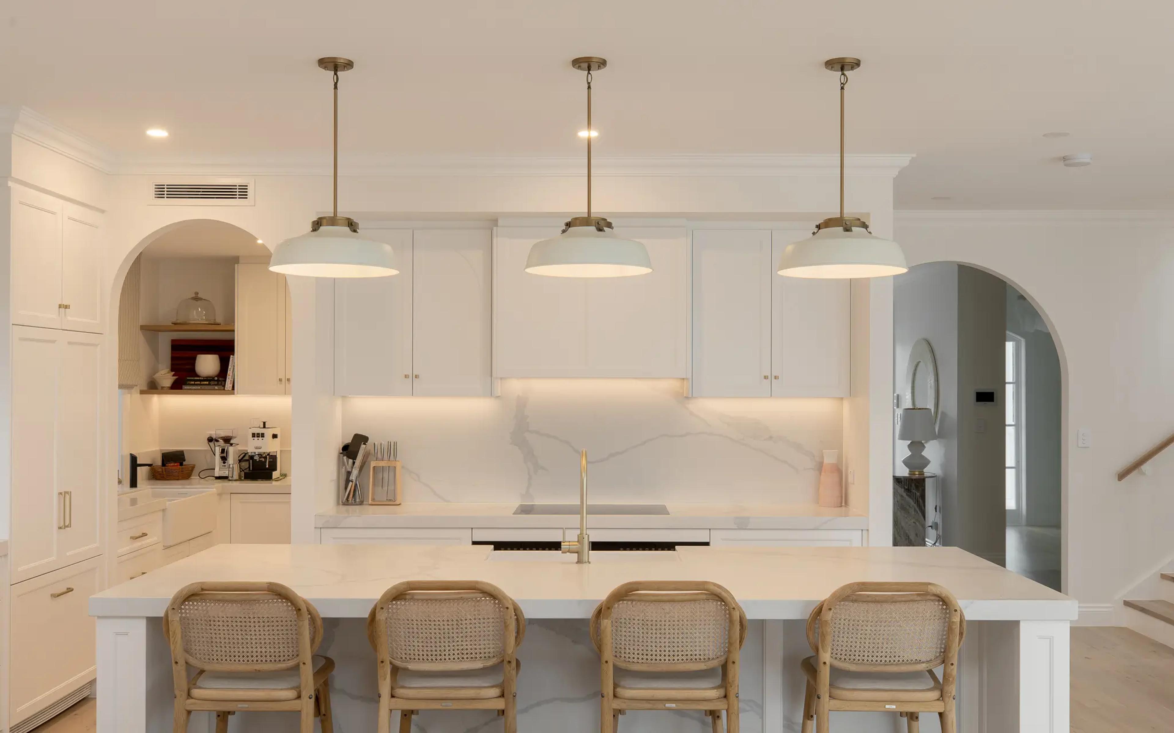 Kitchen island with rattan stools and pendant lights above stone benchtop
