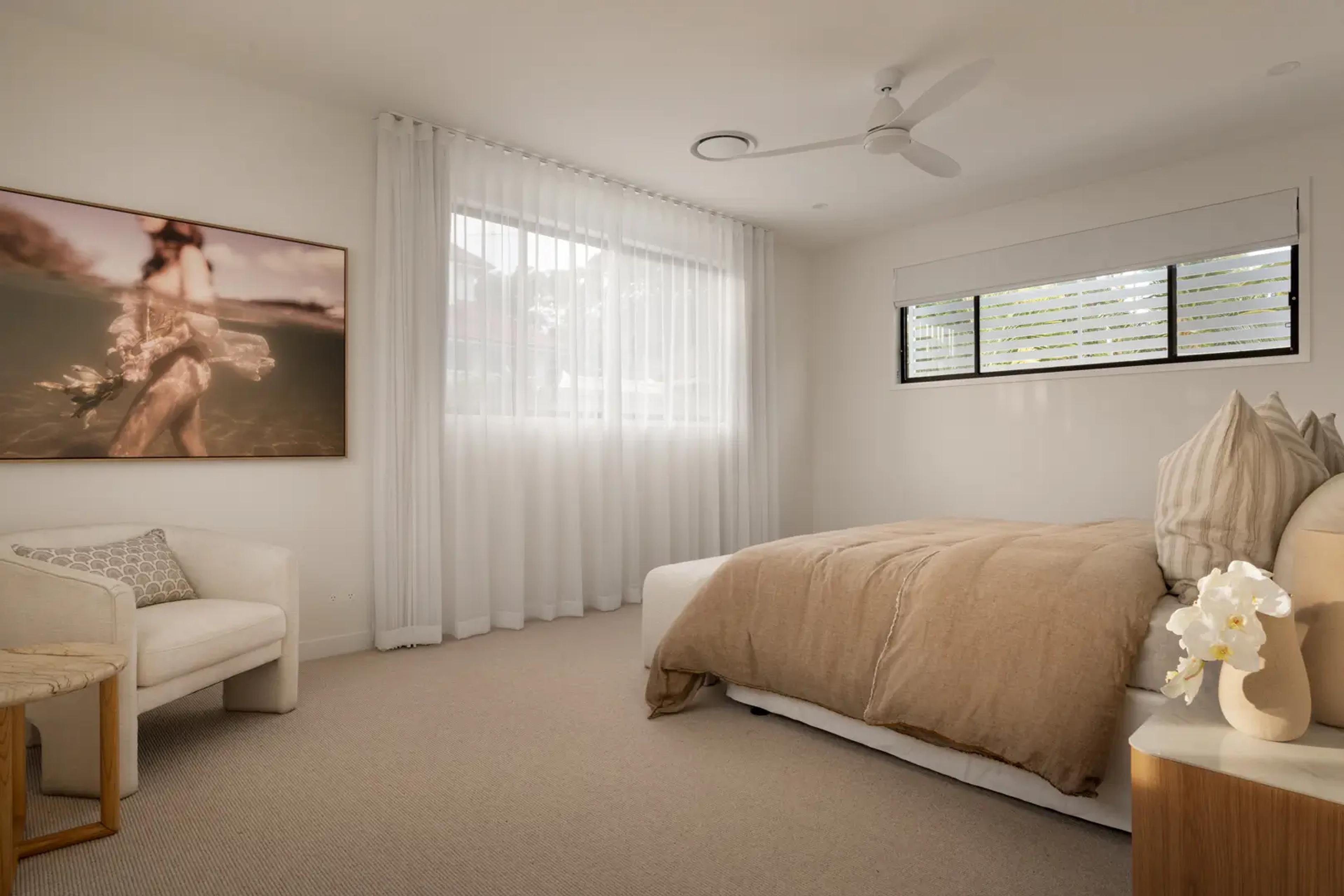 Bedroom with beige bedding, armchair and framed artwork