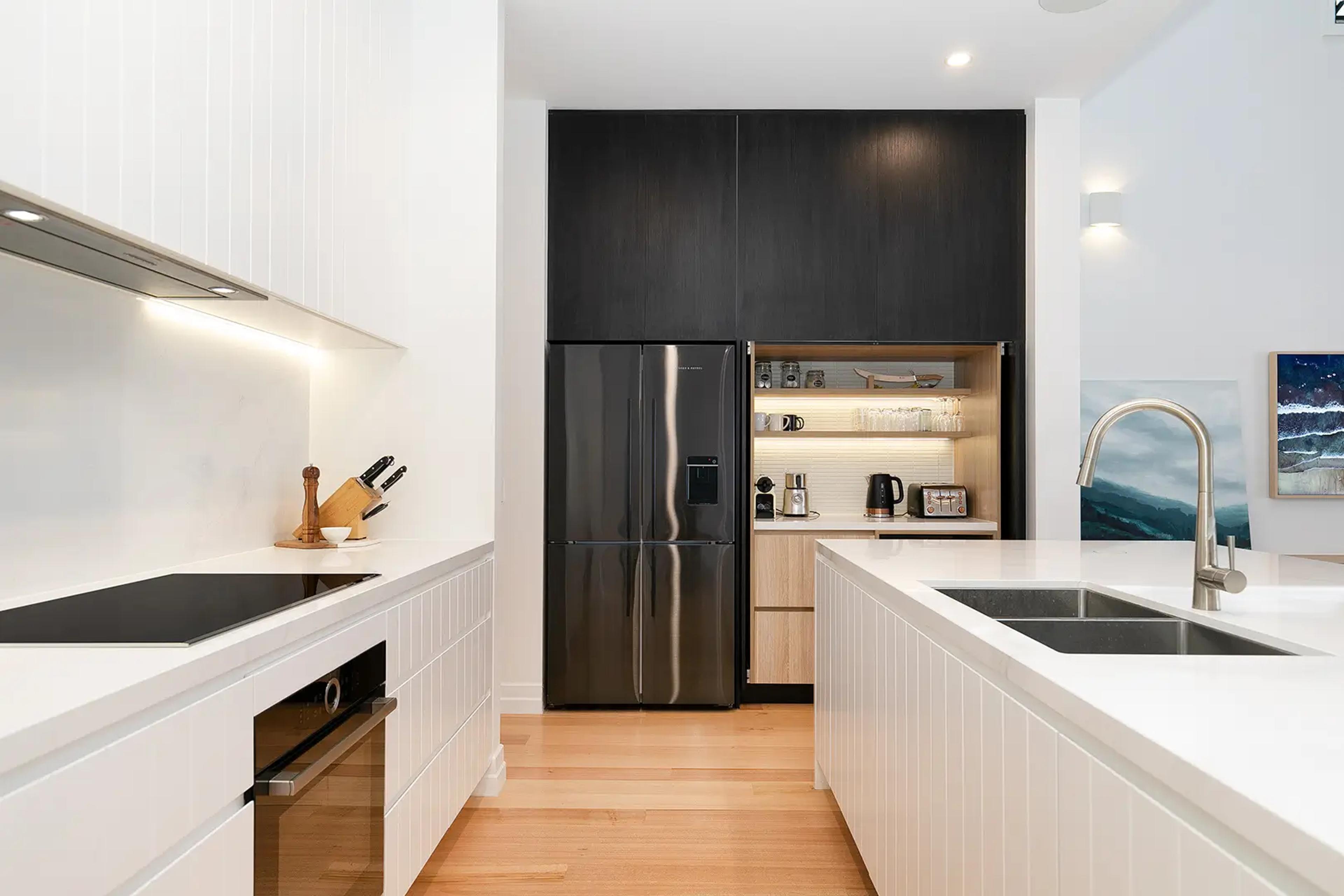 Galley kitchen with white cabinetry and black fridge in pantry recess