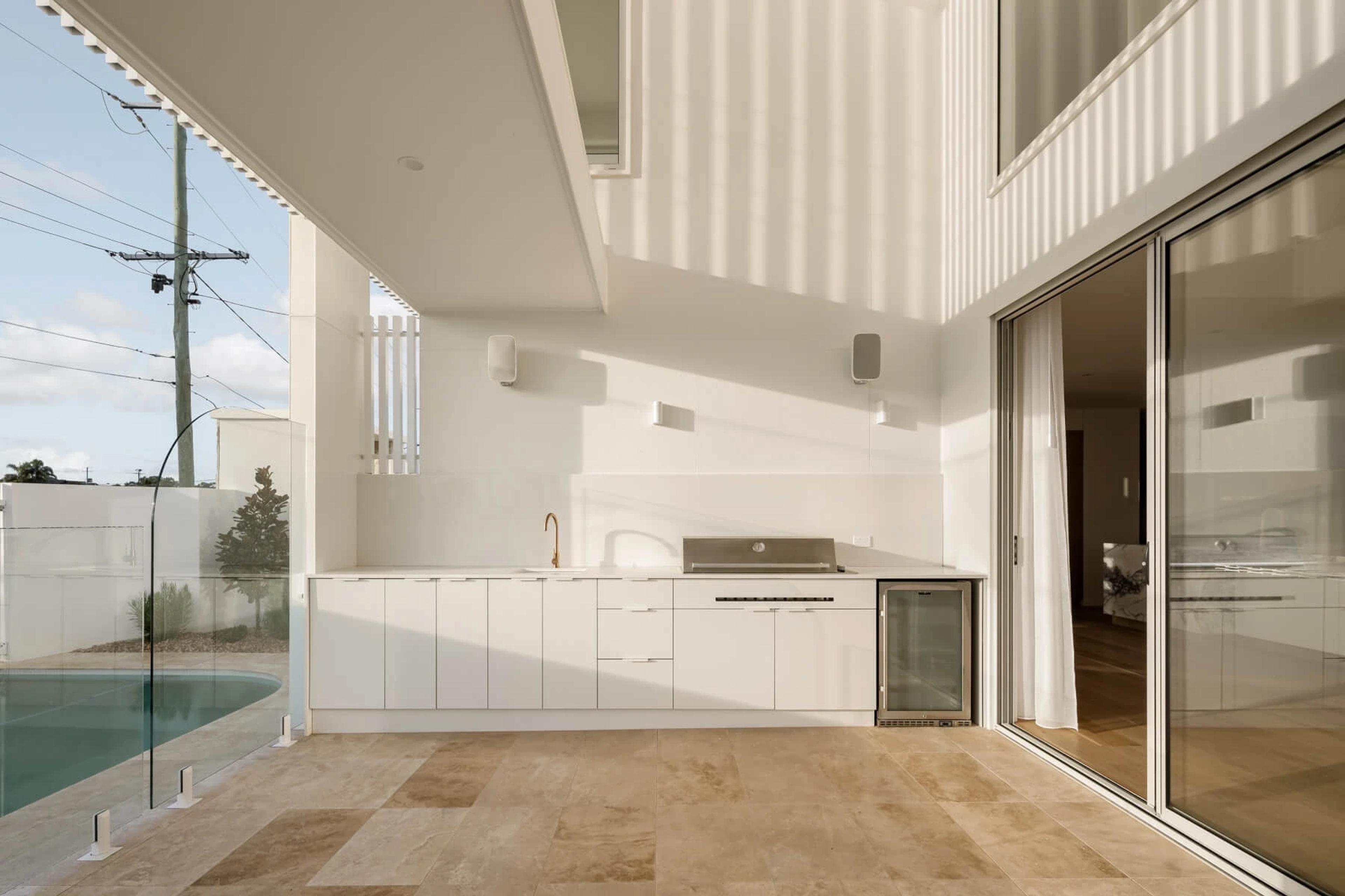 Covered outdoor kitchen beside pool with travertine paving