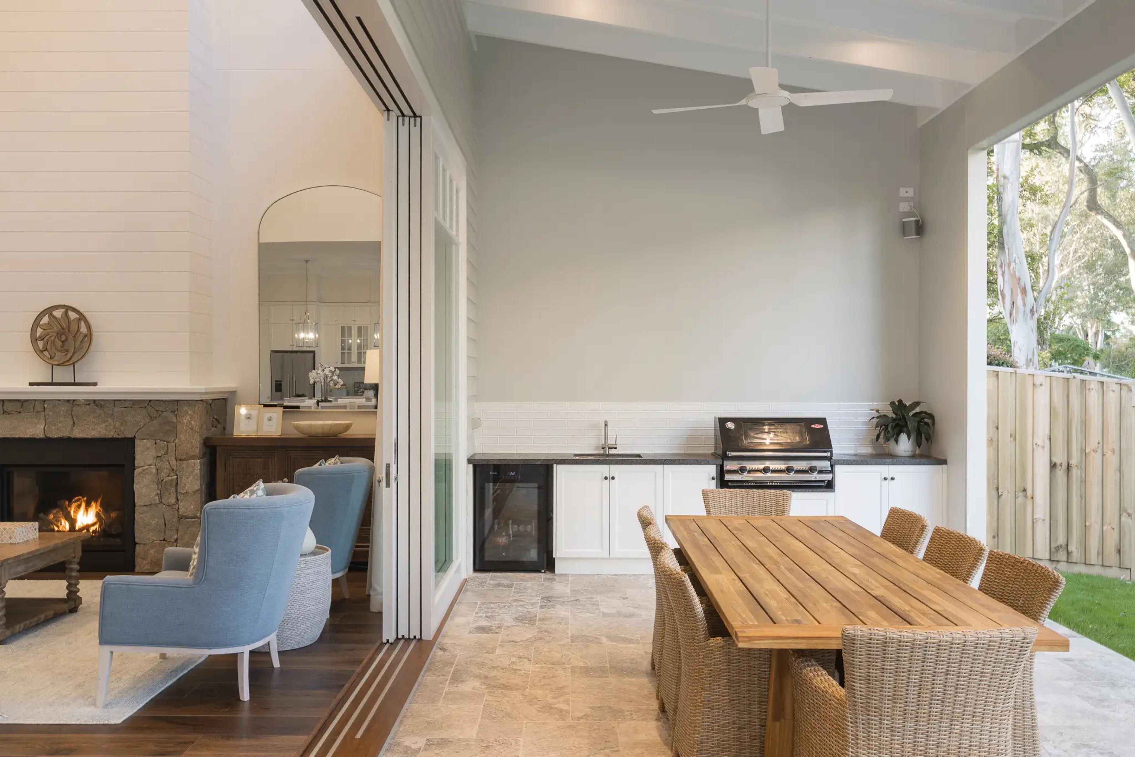 Covered outdoor room with barbecue kitchen, dining table and stone fireplace