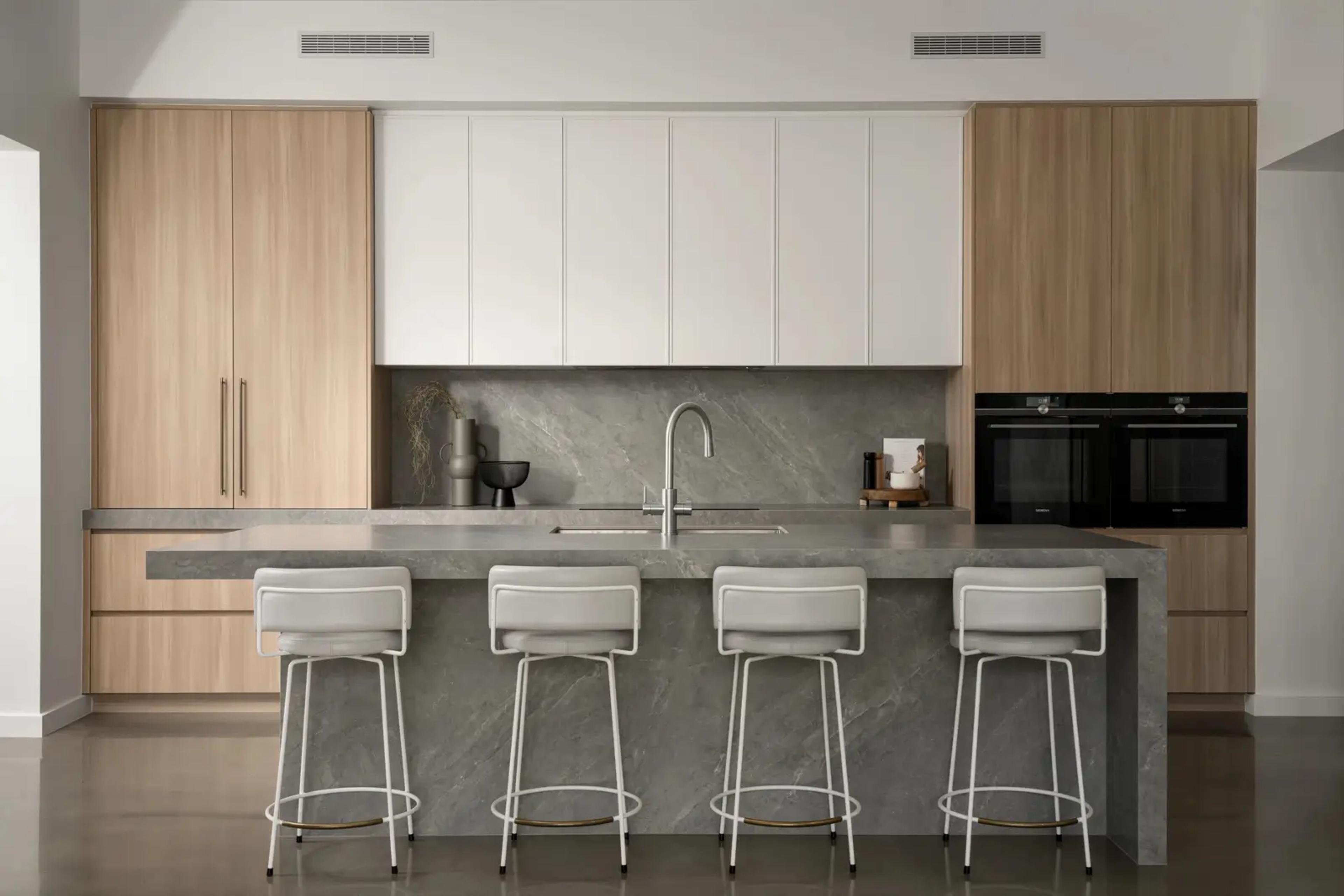 Kitchen with timber cabinetry, stone island and white bar stools