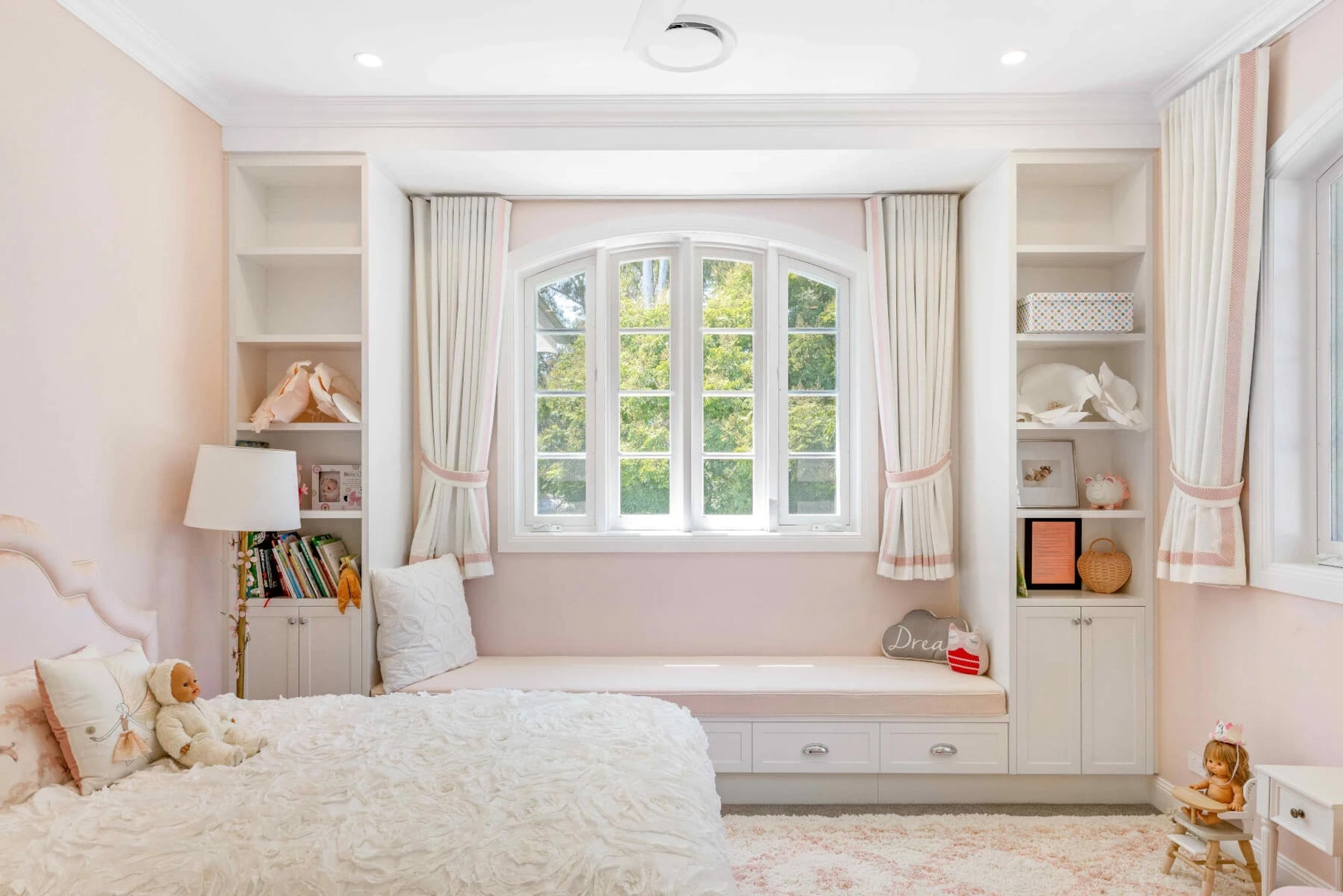 Pink girls bedroom with window seat and built-in shelving