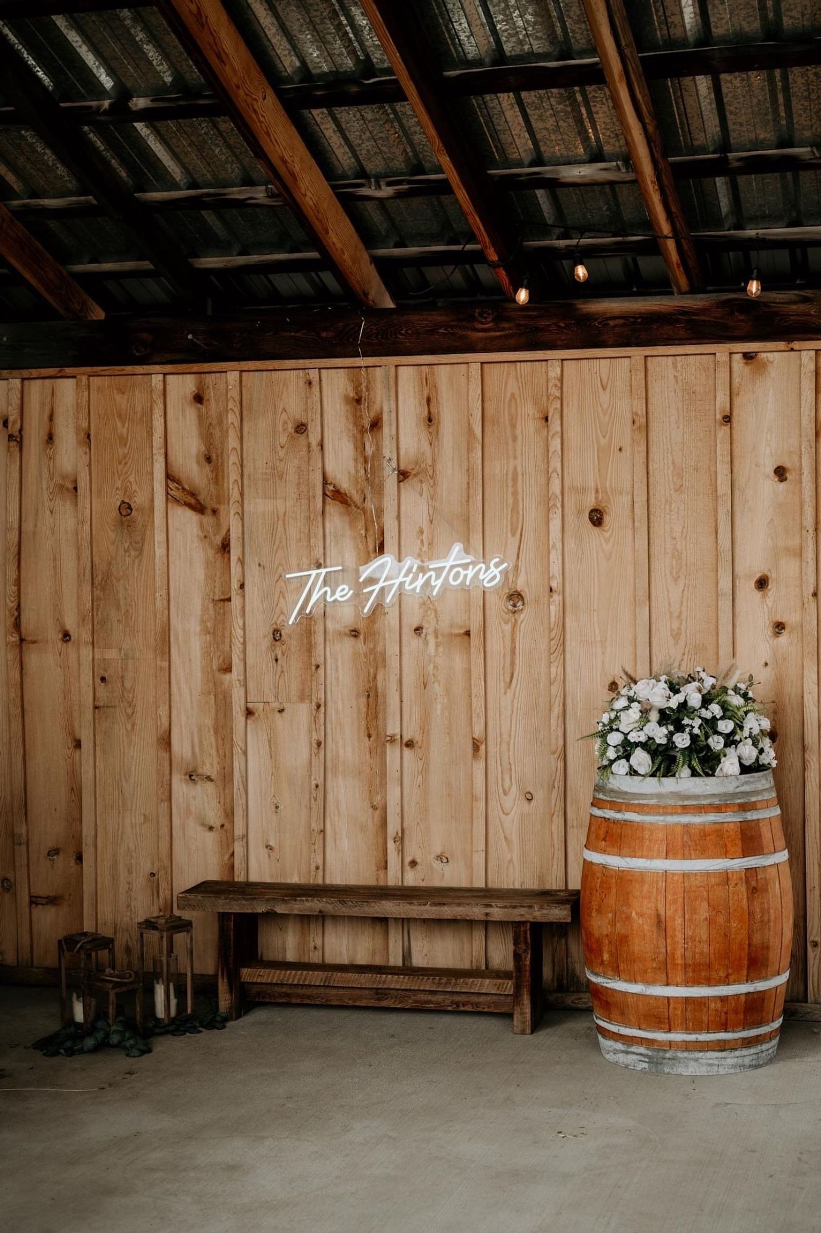Neon last name sign above a bench and a floral-topped barrel
