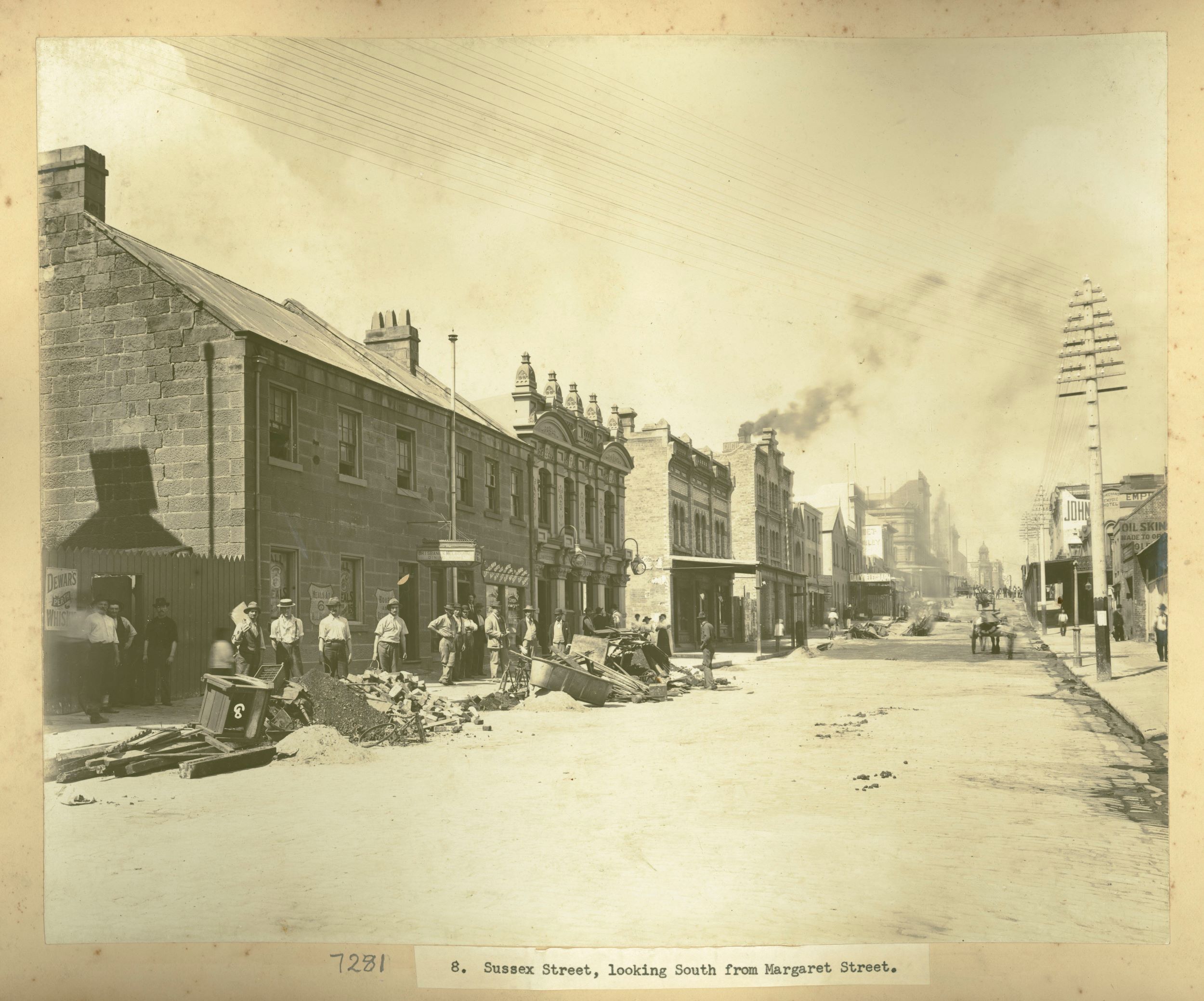 A dirt road with horse and cart and workmen to the side where piles of rubble and rubbish have been dropped.