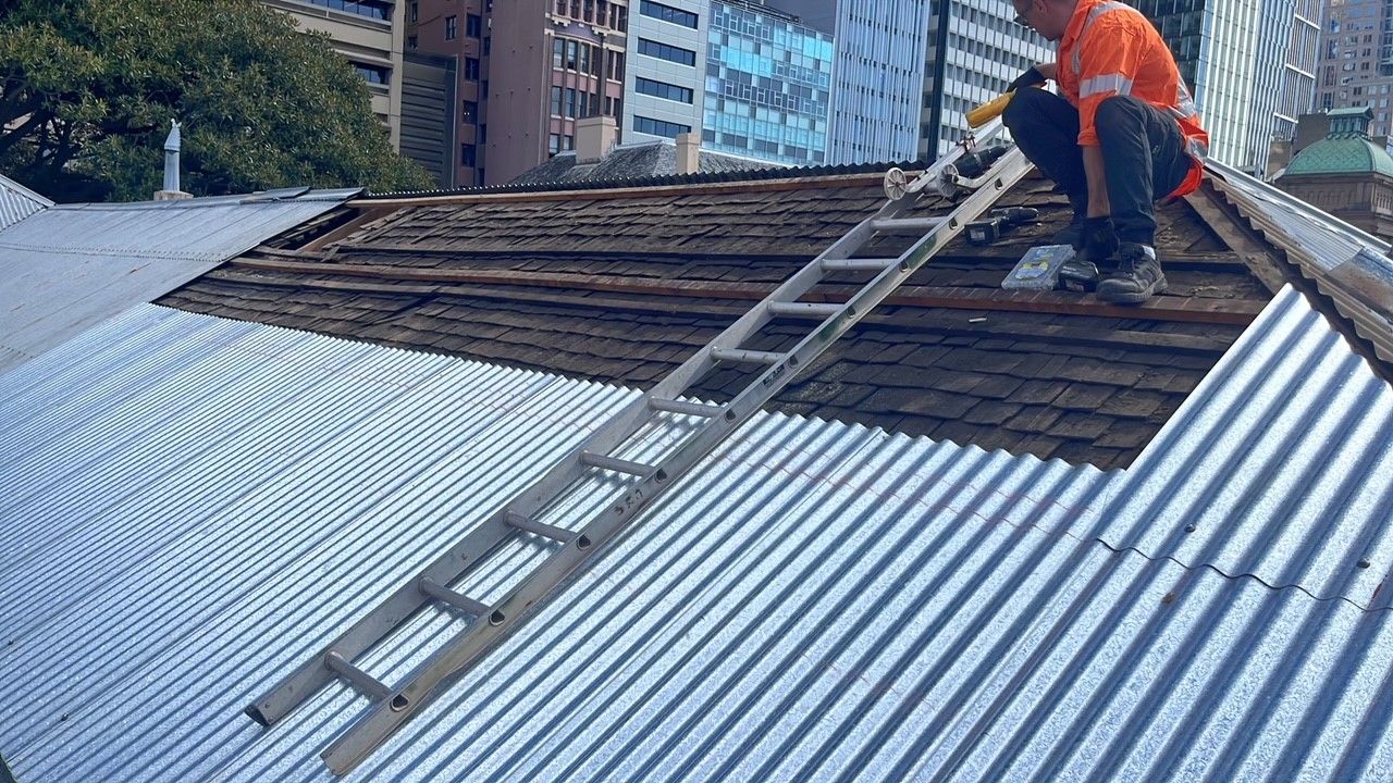 A man holds a ladder on a roof that is under repair